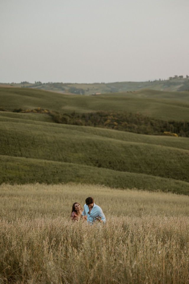 Couple sitting in golden field with rolling hills and countryside landscape.