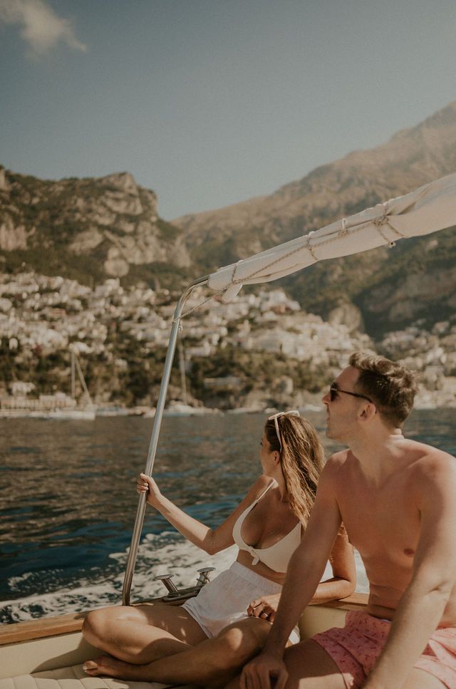 Couple relaxing on sailboat along Amalfi Coast's dramatic cliffs.