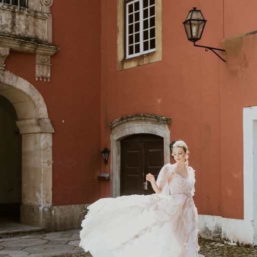 Elegant bride twirling in lace dress against terracotta walls and stone architecture.