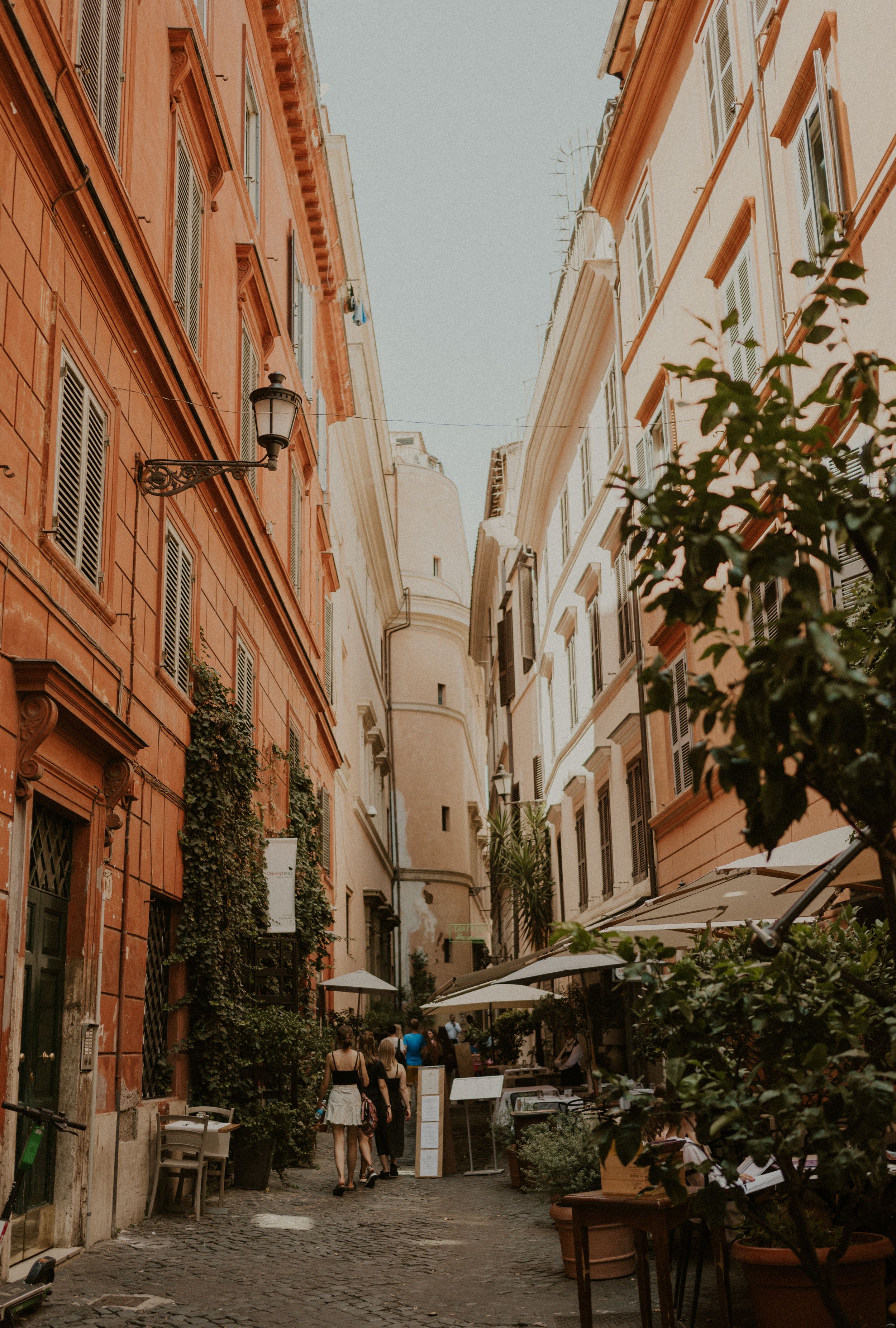 Narrow cobblestone street in Rome with traditional architecture and outdoor cafe seating.