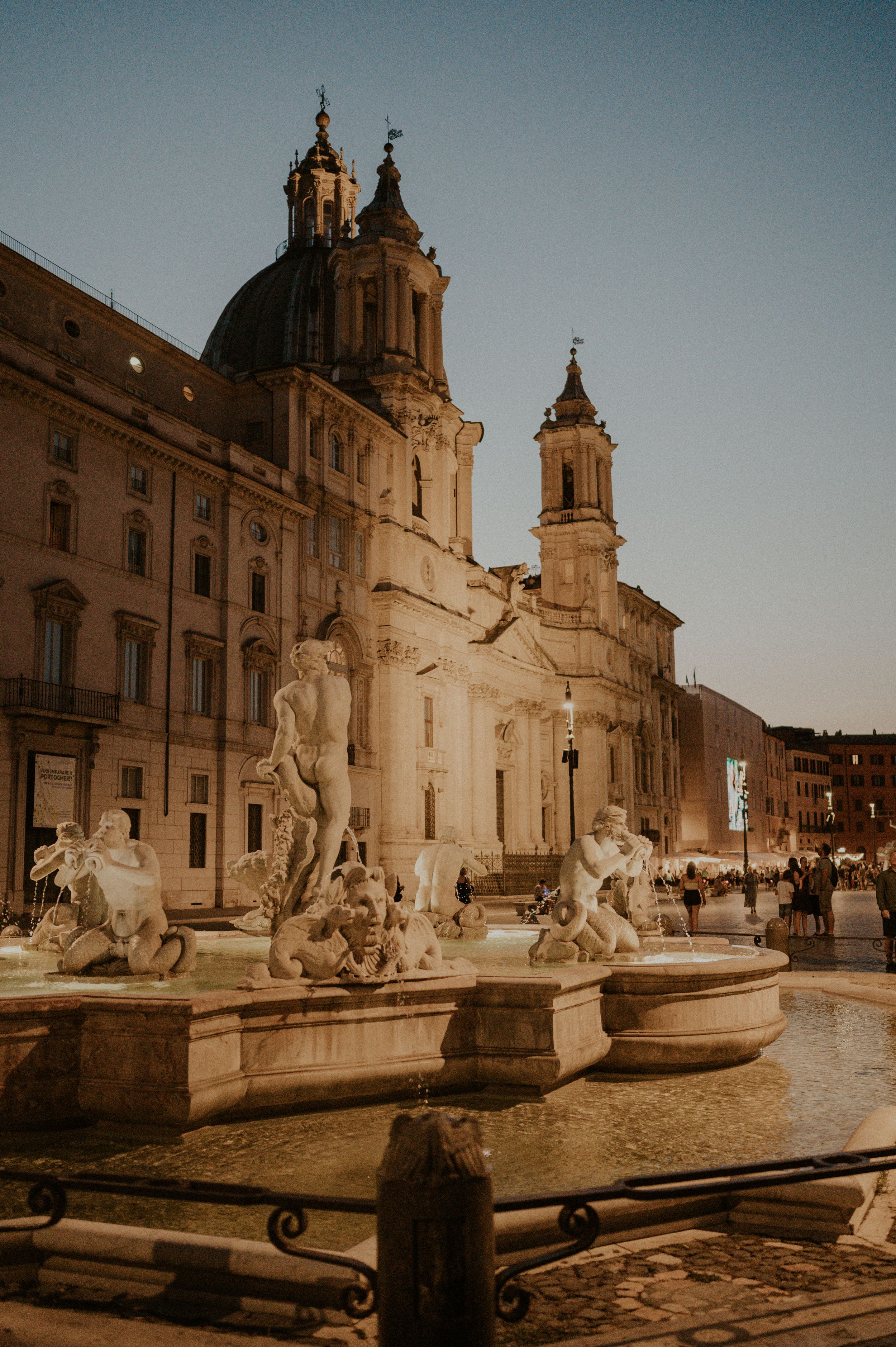 Historic Piazza Navona in Rome with Baroque church and ornate fountains at sunset.