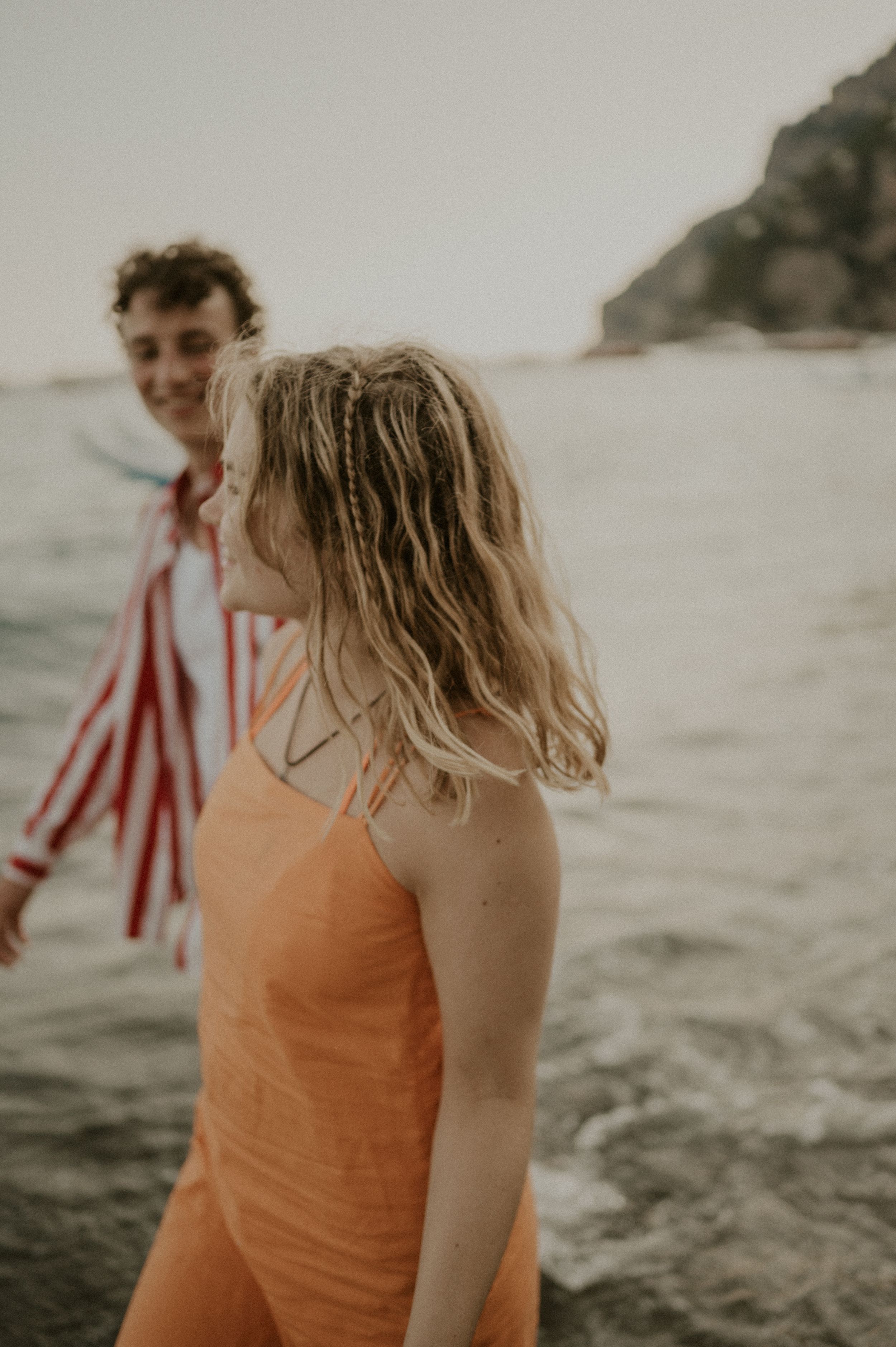 A couple enjoys a playful moment by the ocean wearing contrasting orange and red striped outfits.