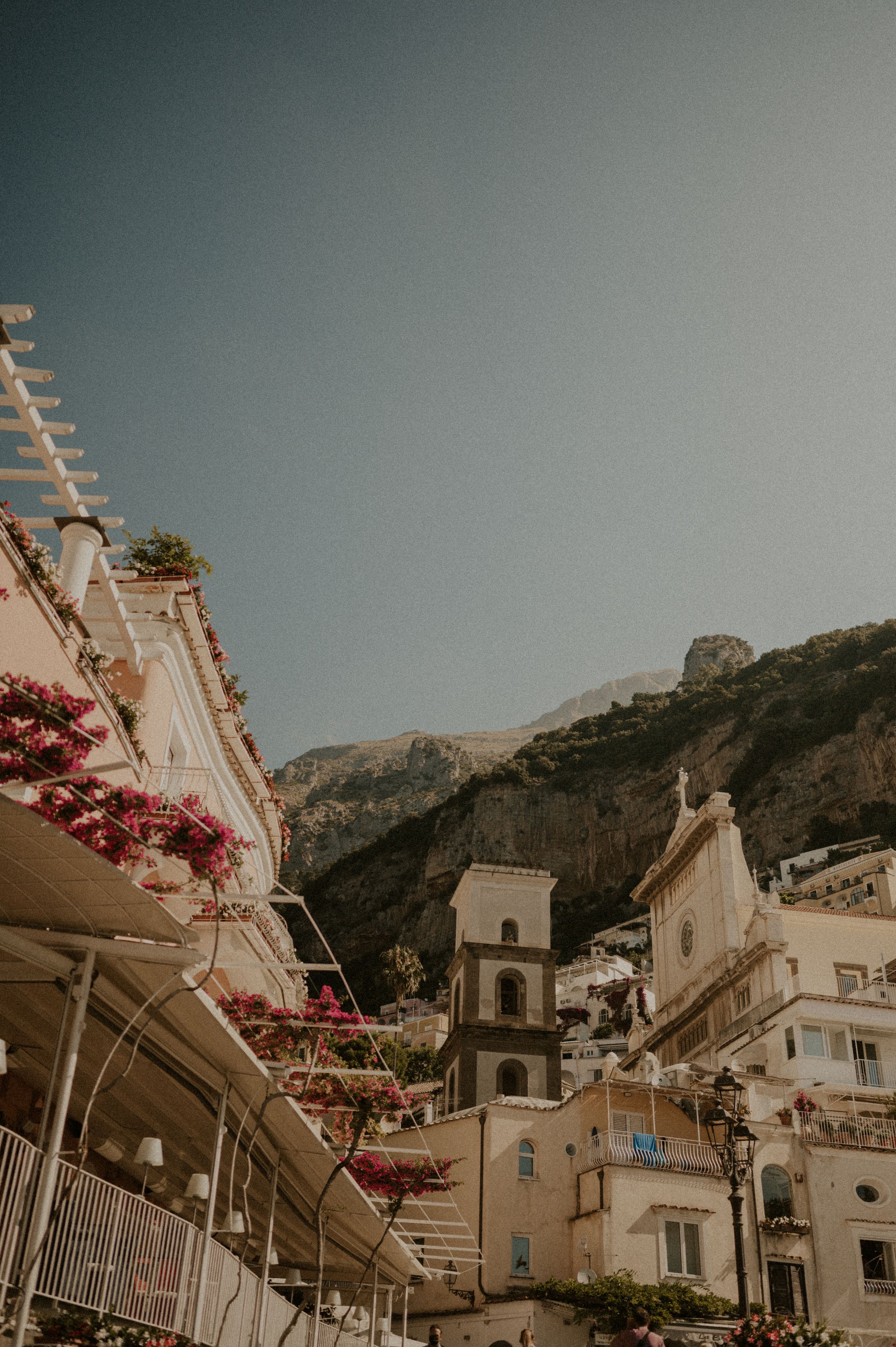 Historic church tower and buildings with flowering vines along the steep streets of Positano.