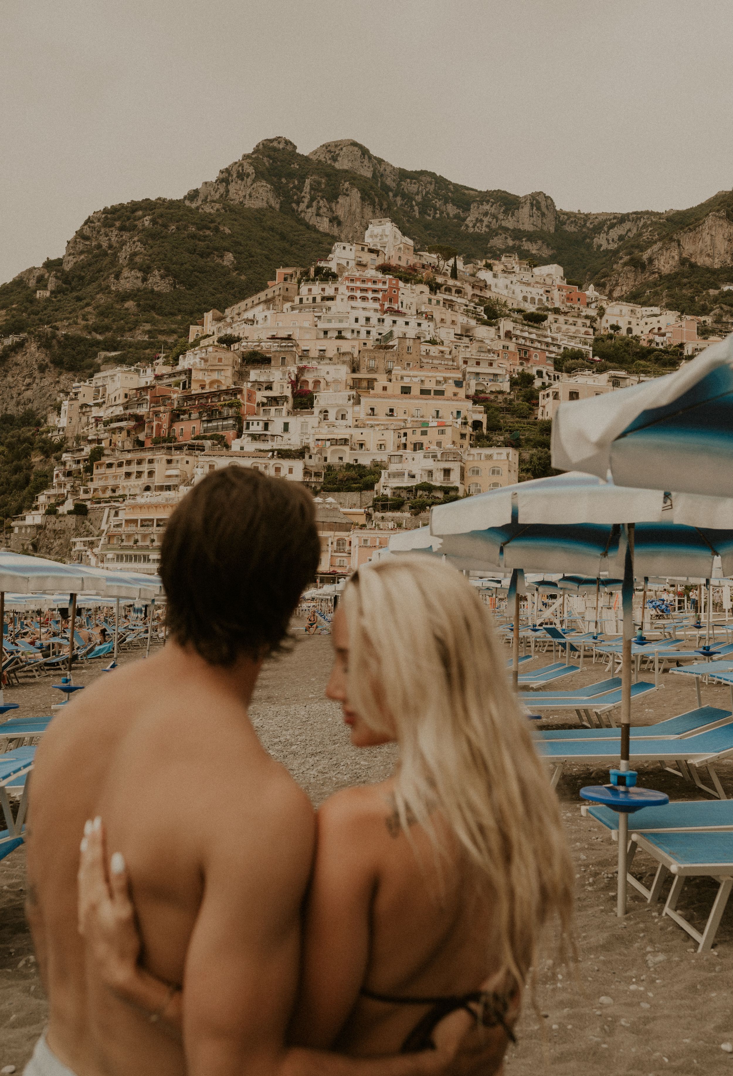 Scenic view of Positano's cascading architecture on hillside with beach umbrellas in foreground.