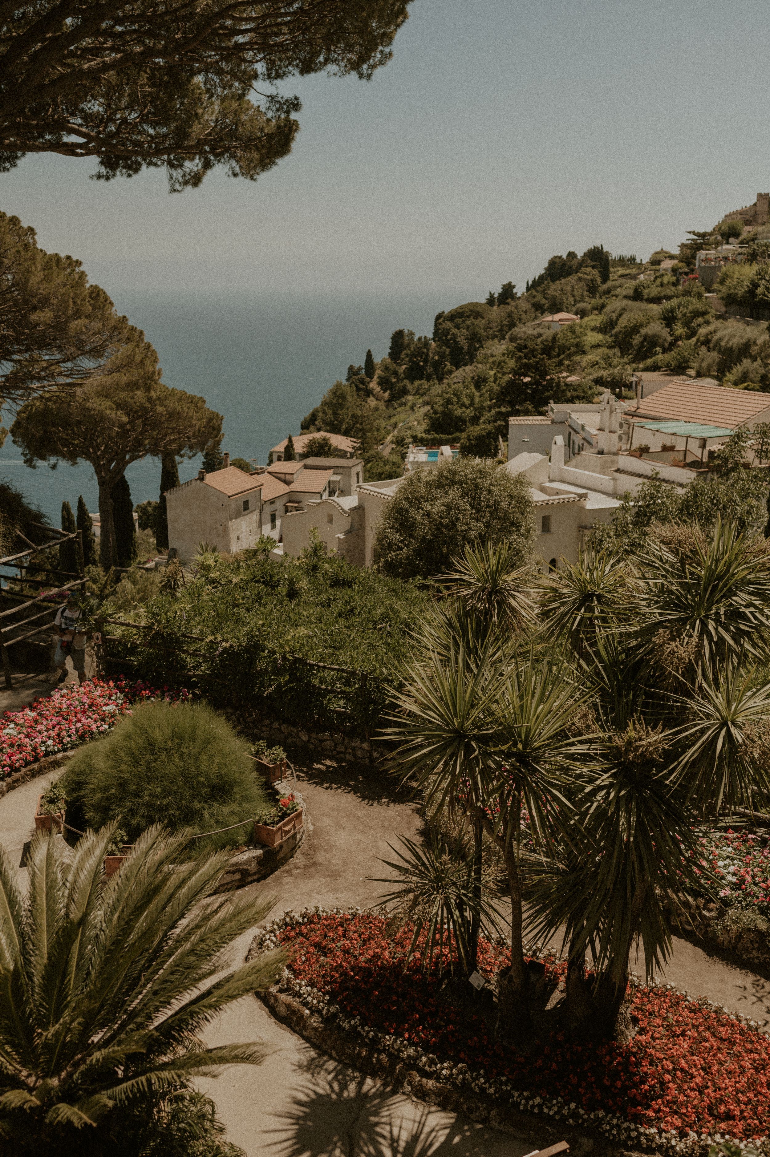 Scenic coastal view of Mediterranean hillside villas with lush gardens and palm trees overlooking the sea.