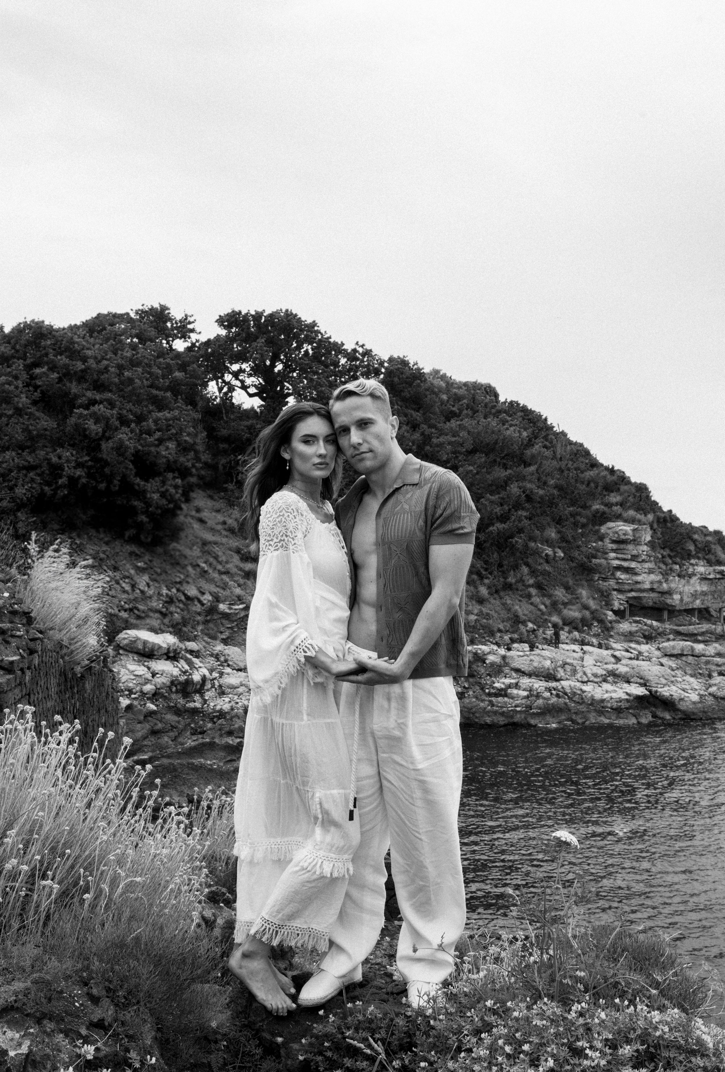 Black and white portrait of couple against coastal backdrop with natural vegetation.