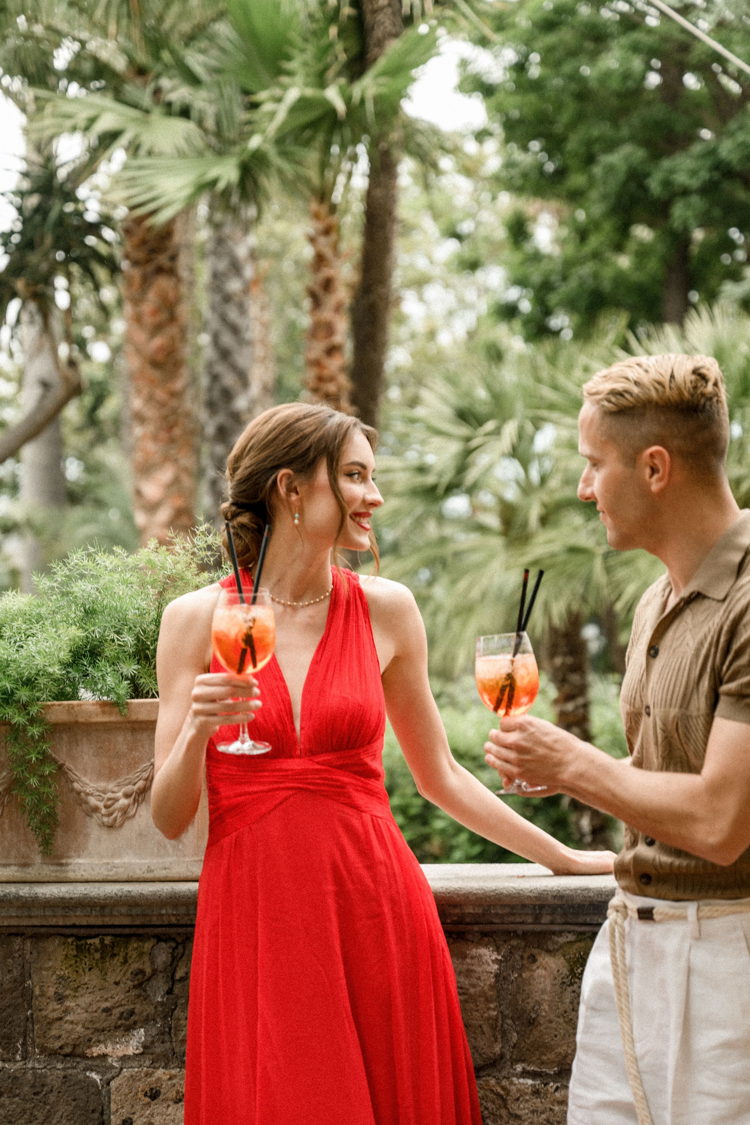 A couple enjoys cocktails in a tropical garden setting.