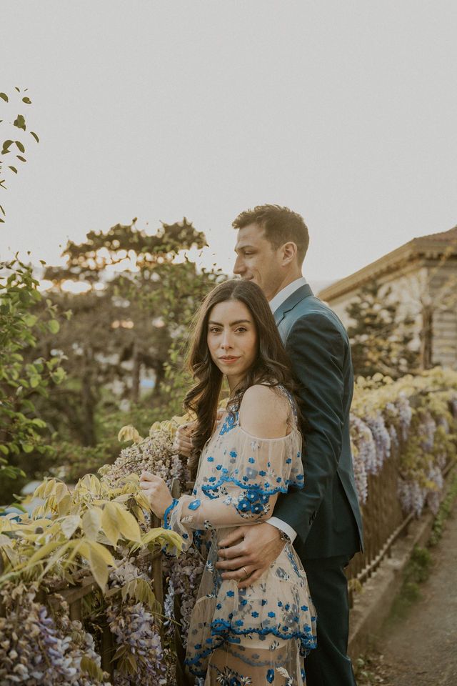 Intimate portrait of couple embracing in garden with floral dress and formal attire.