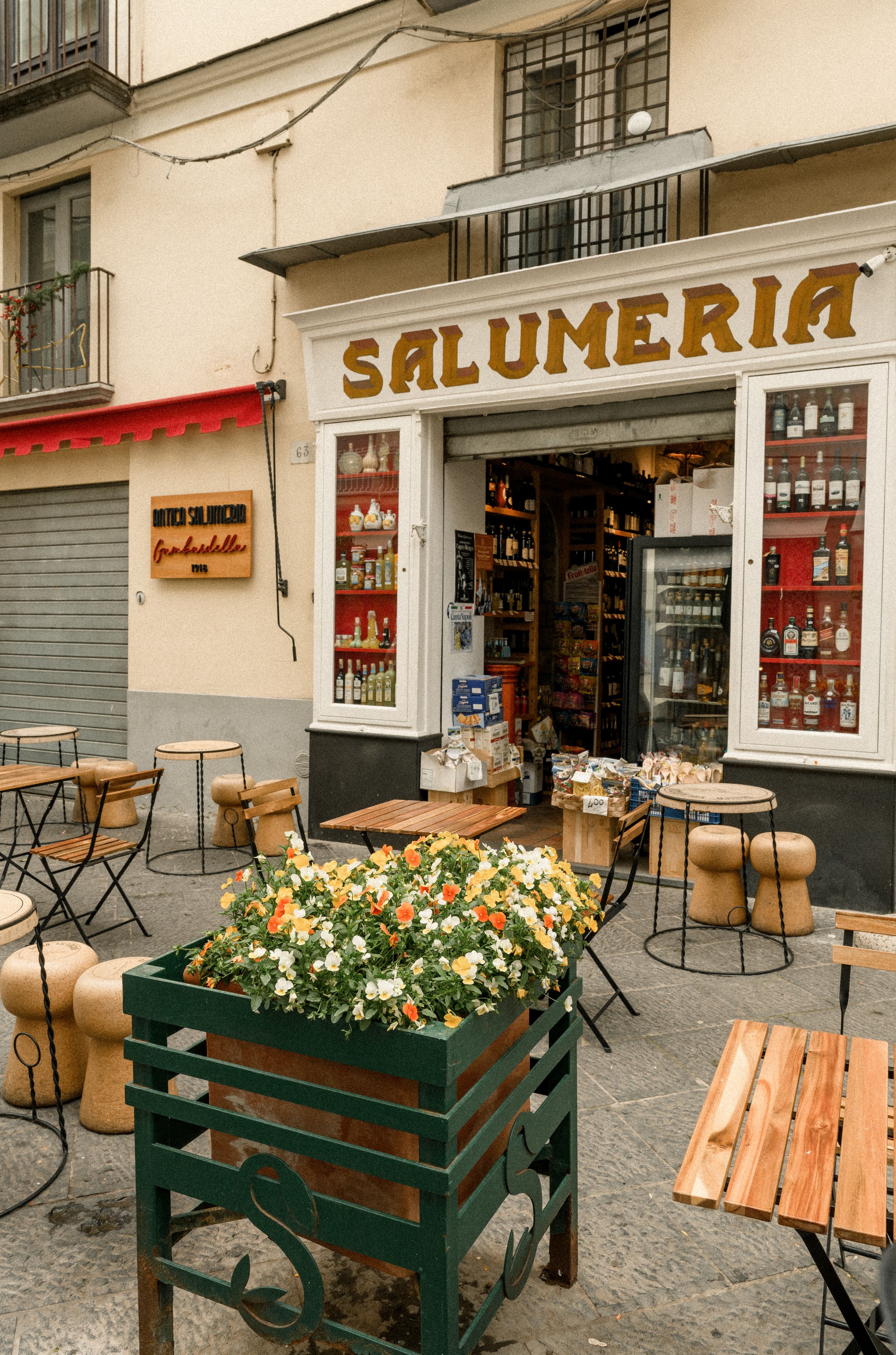 Charming salumeria storefront with outdoor seating and flowering planters on the street.