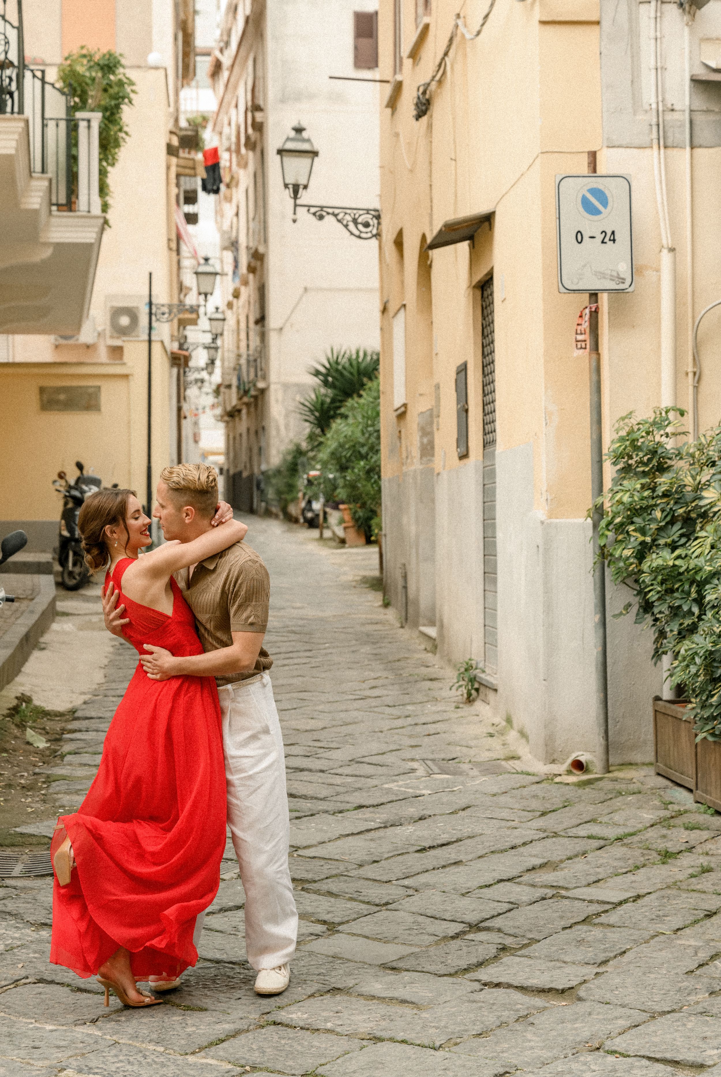 Couple dancing in narrow Italian alleyway with red dress flowing dramatically.