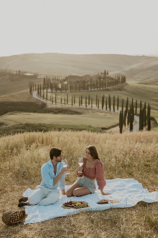 Couple enjoying intimate picnic on blanket overlooking rolling Tuscan hills.