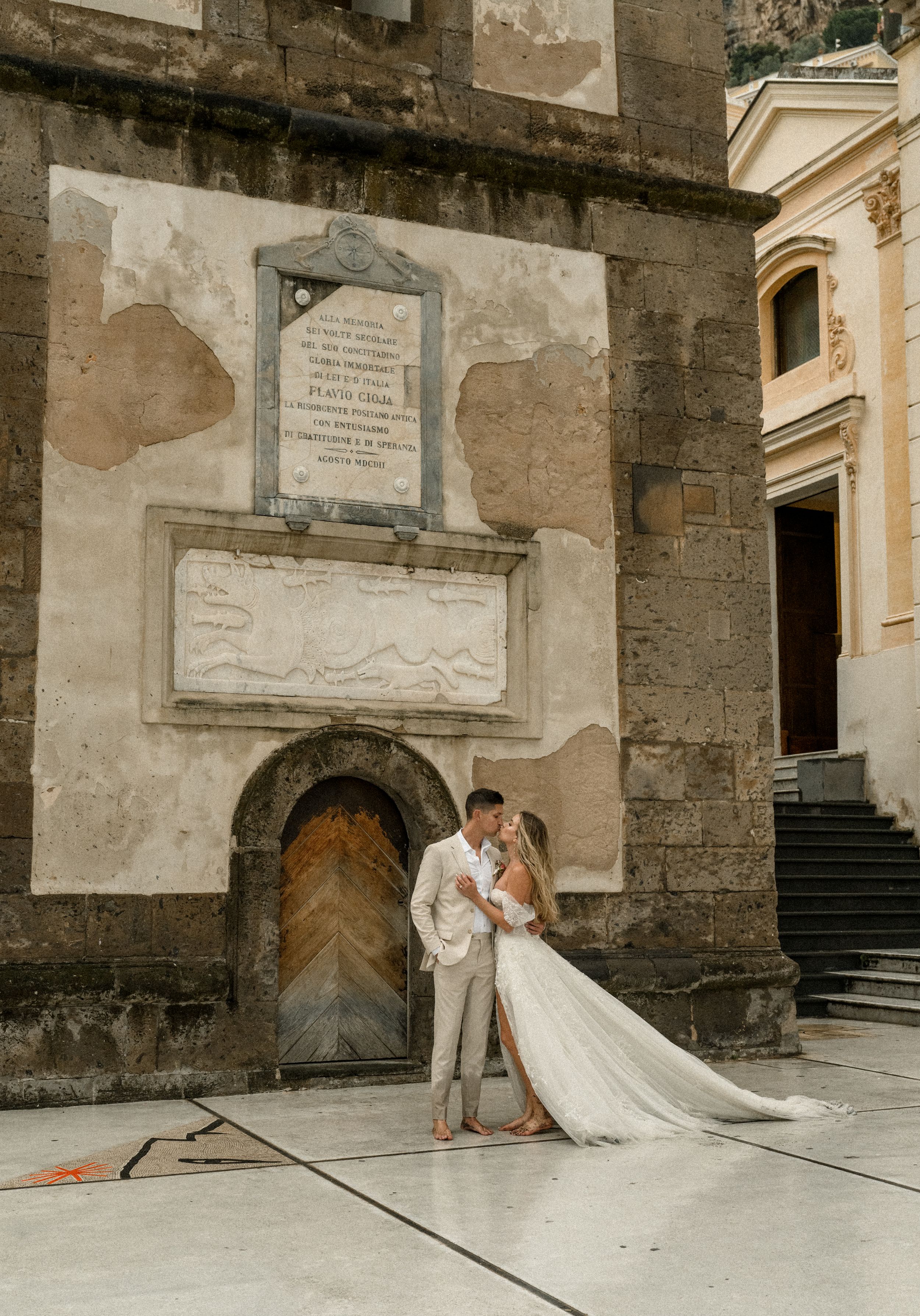 A couple poses in front of an ancient stone church wall with architectural details and inscriptions.