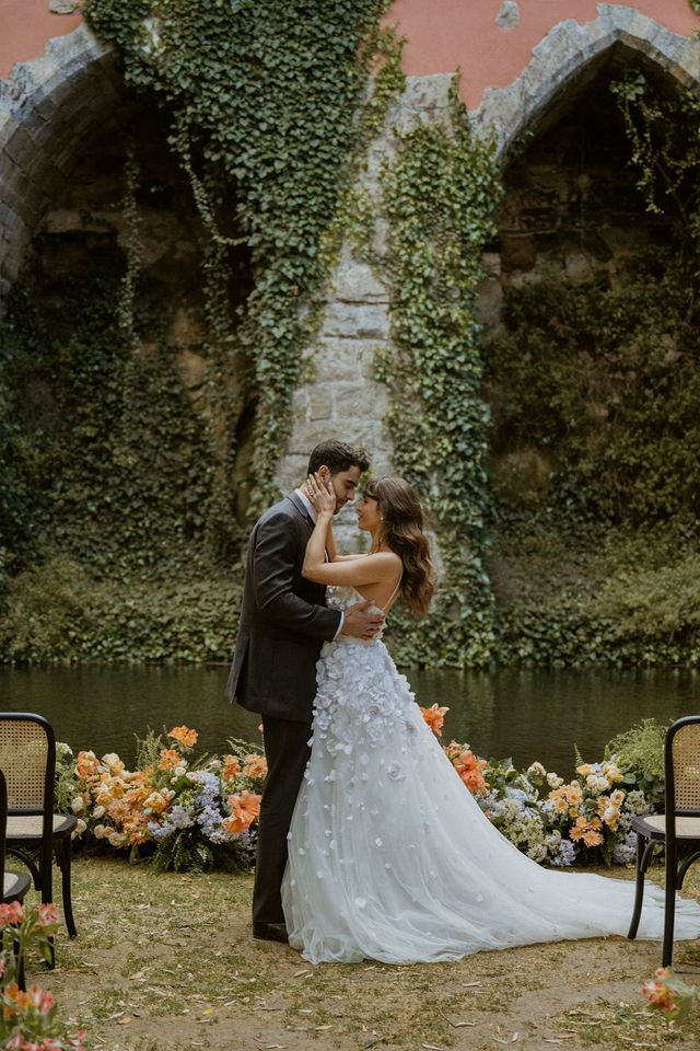 Wedding ceremony setup with floral arrangements by ivy-covered stone wall and reflecting pool.