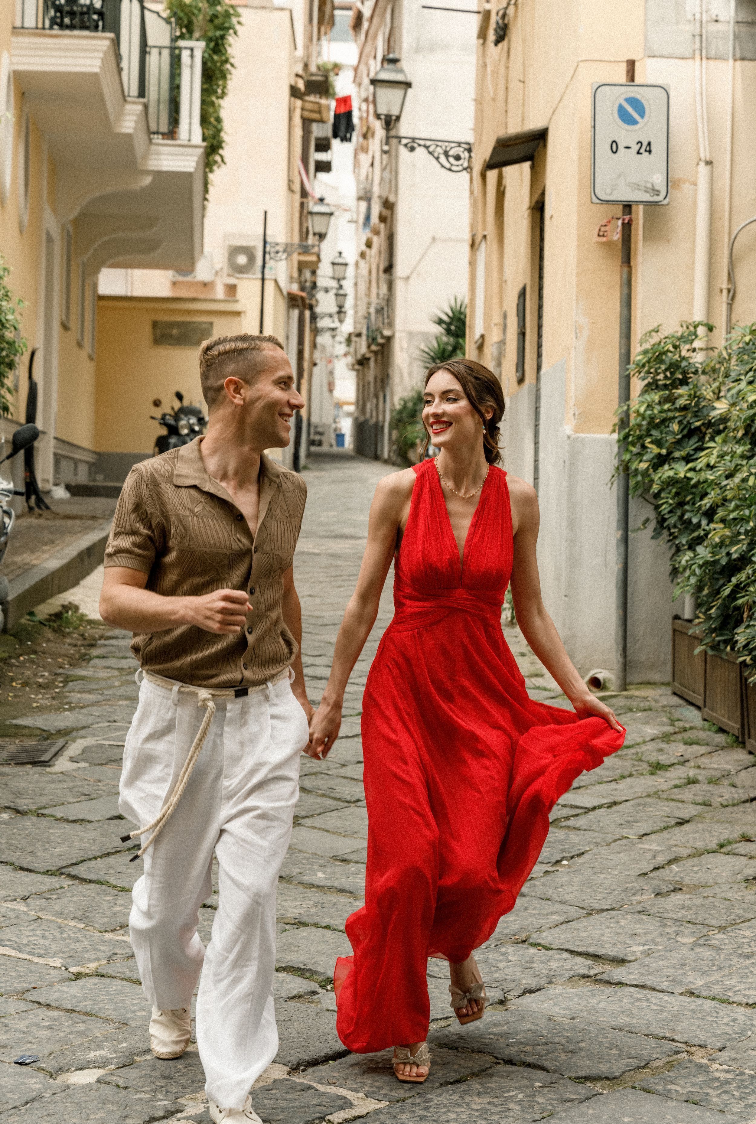A couple walks through narrow Italian streets while wearing summer attire.