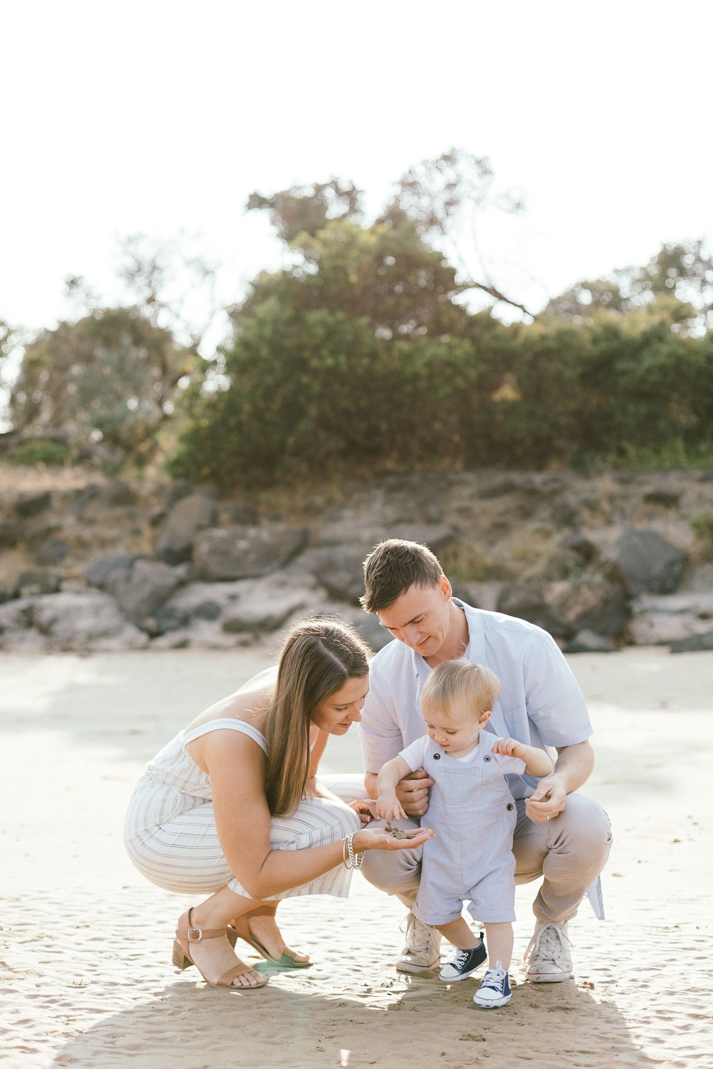 Family kneeling together on sandy beach during golden hour portrait session.