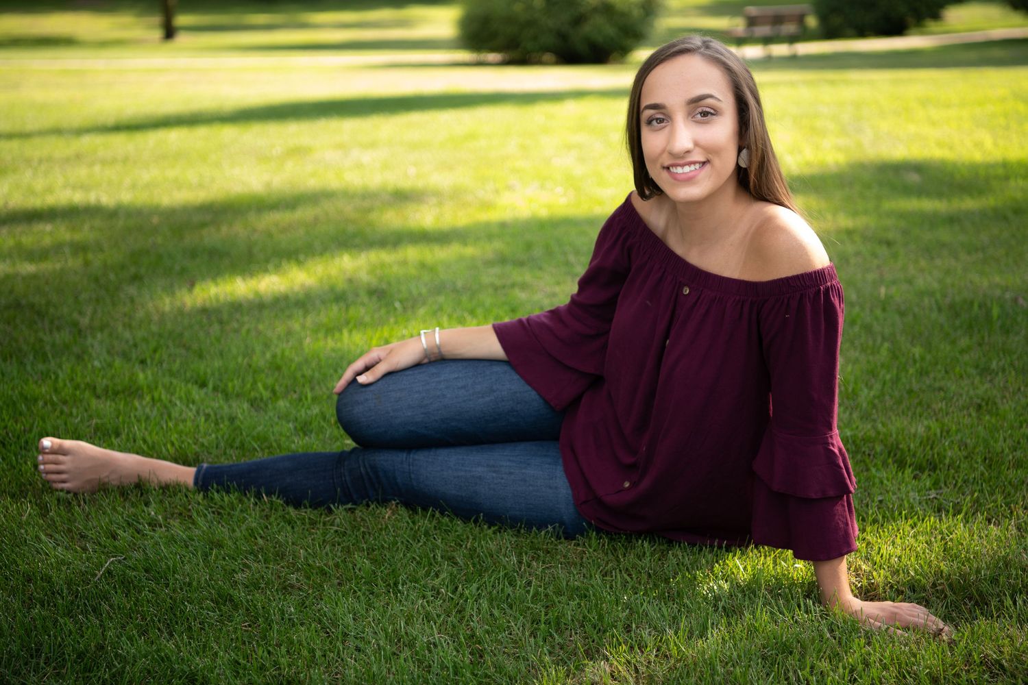 A casual outdoor portrait on grass wearing a burgundy off-shoulder top and jeans.
