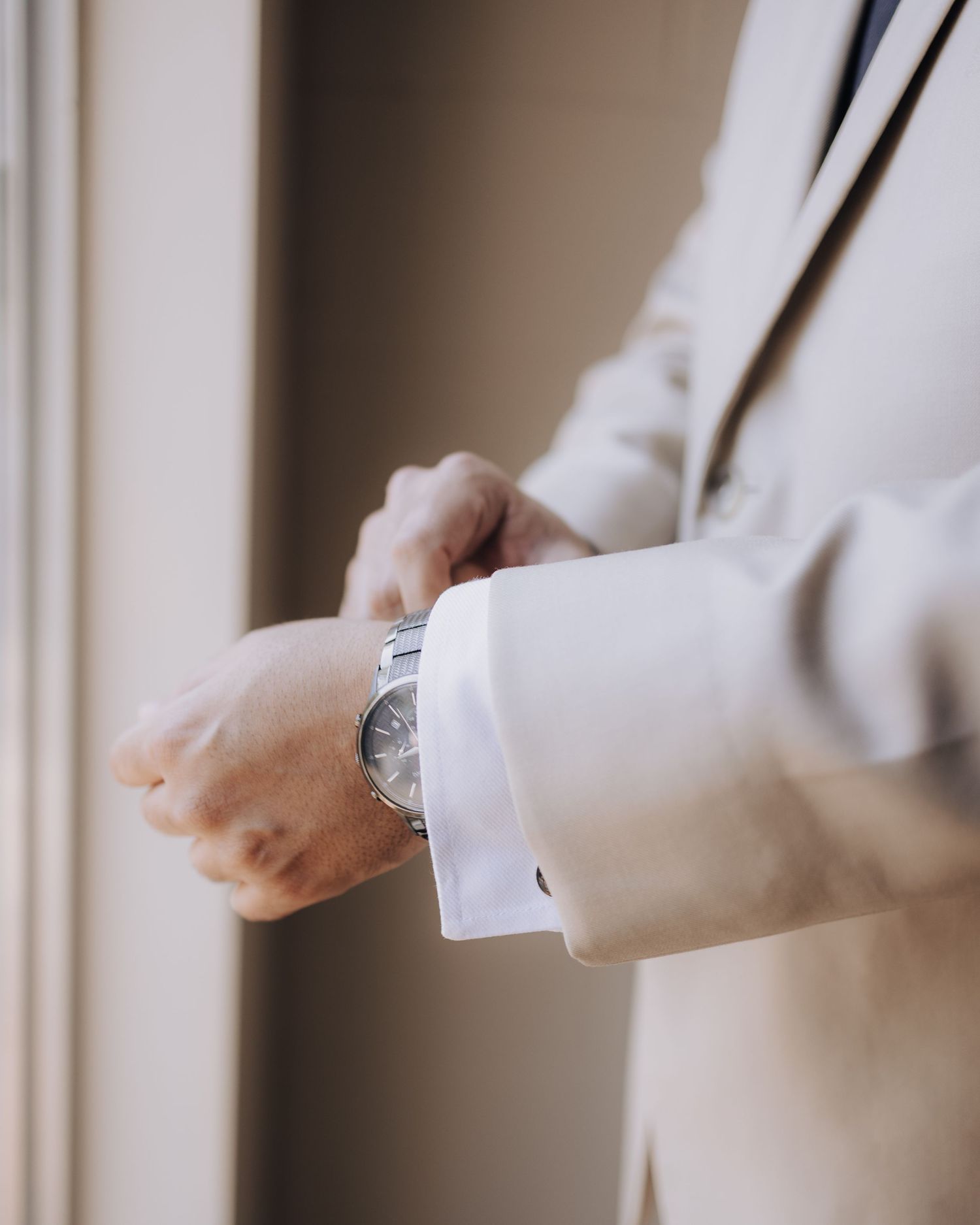 Close-up of hands adjusting a watch while wearing a light colored formal suit jacket.