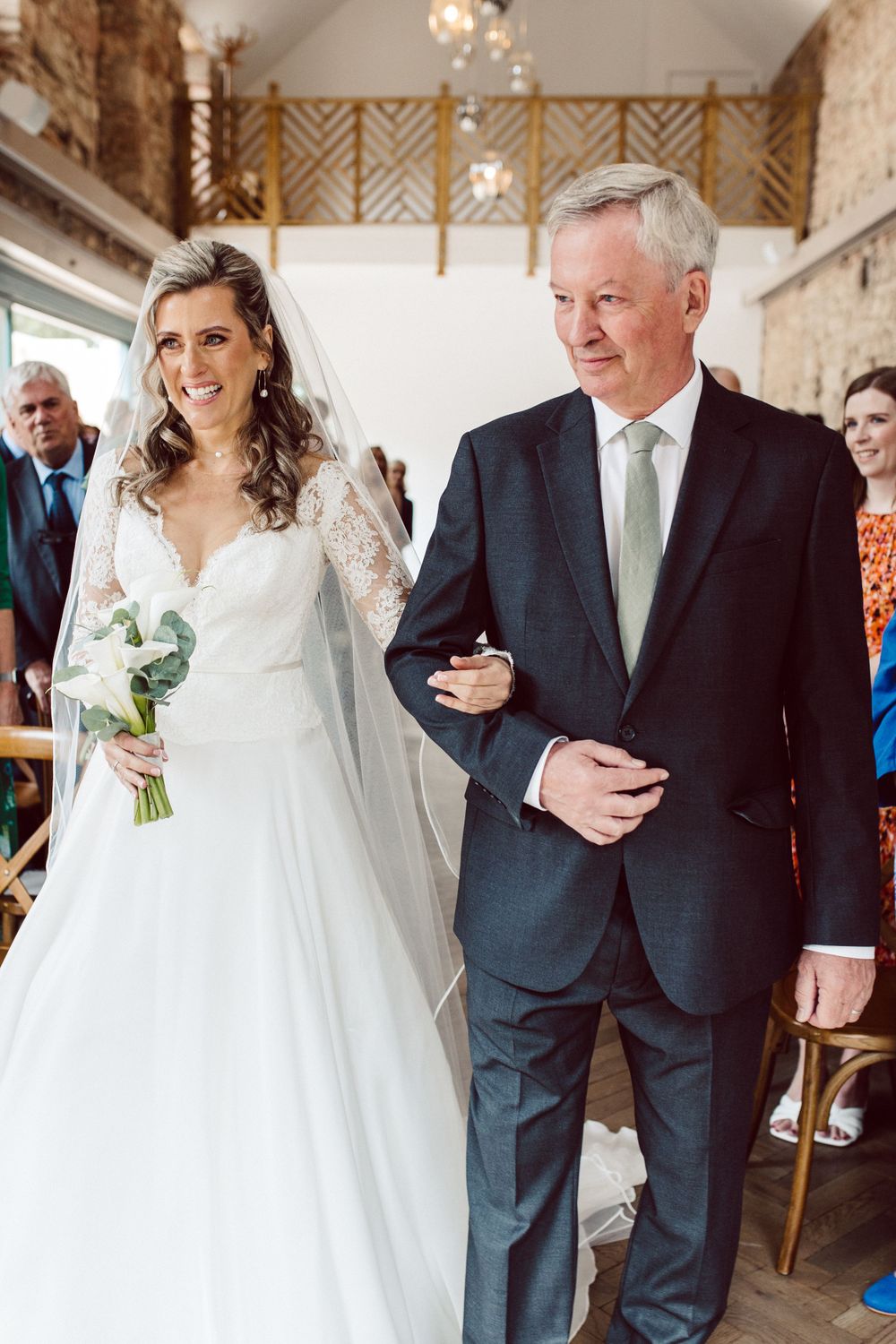 A wedding processional in a bright indoor venue with stone walls and wooden accents.