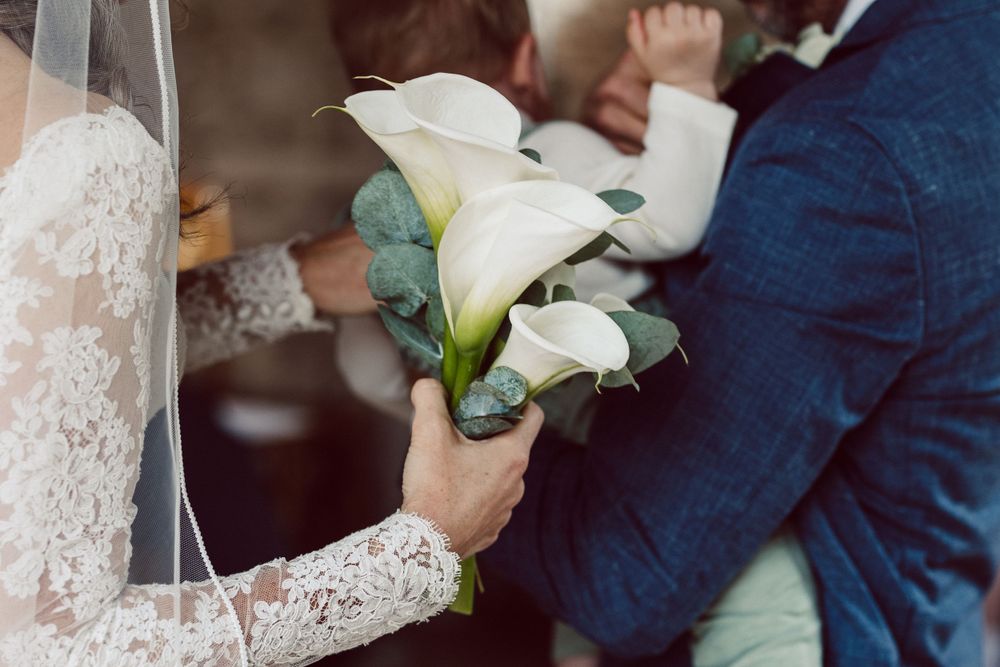 White calla lily bouquet with greenery against formal wedding attire.