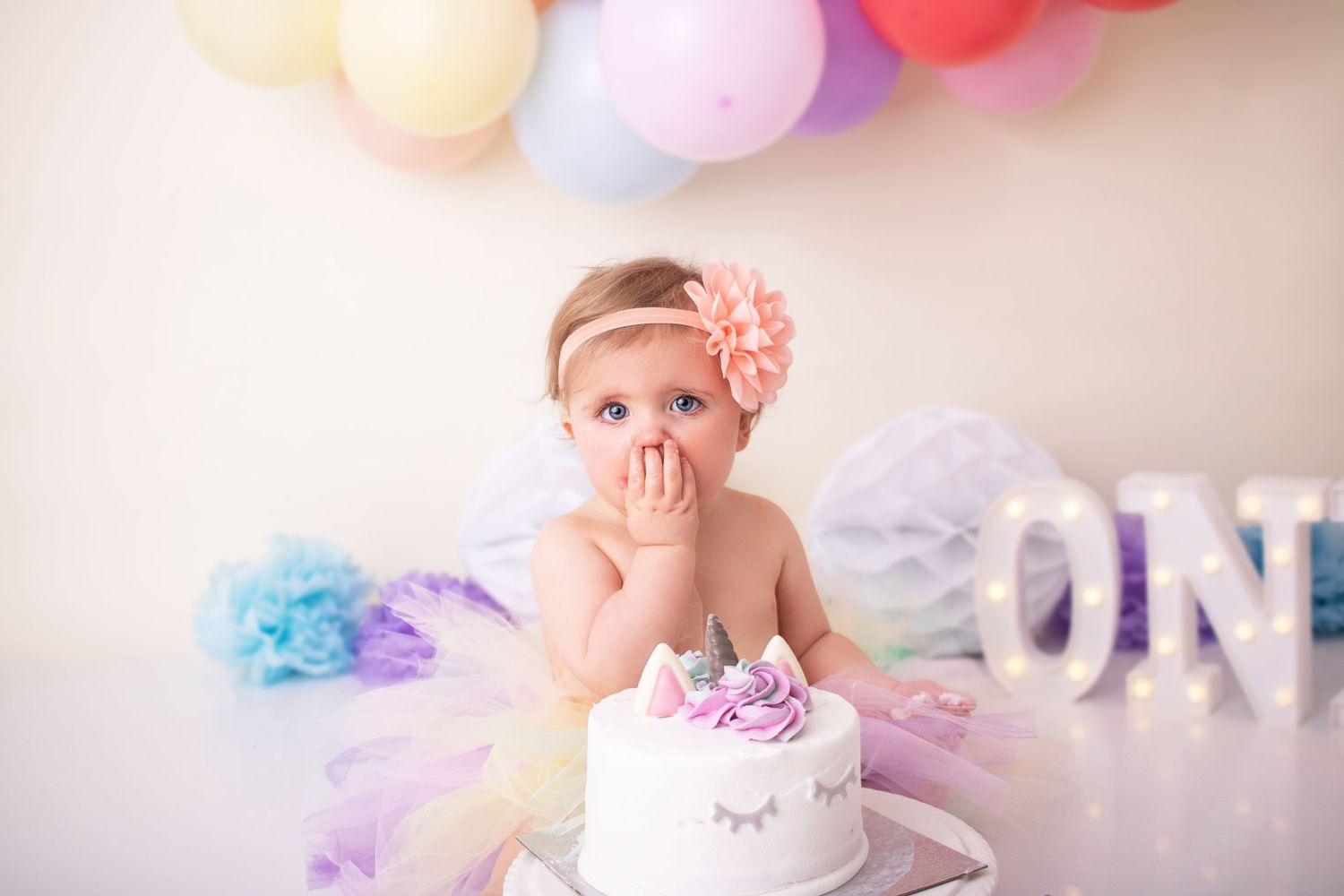 baby girl at her cake smash with hand near mouth photographed by cake smash photographer swansea