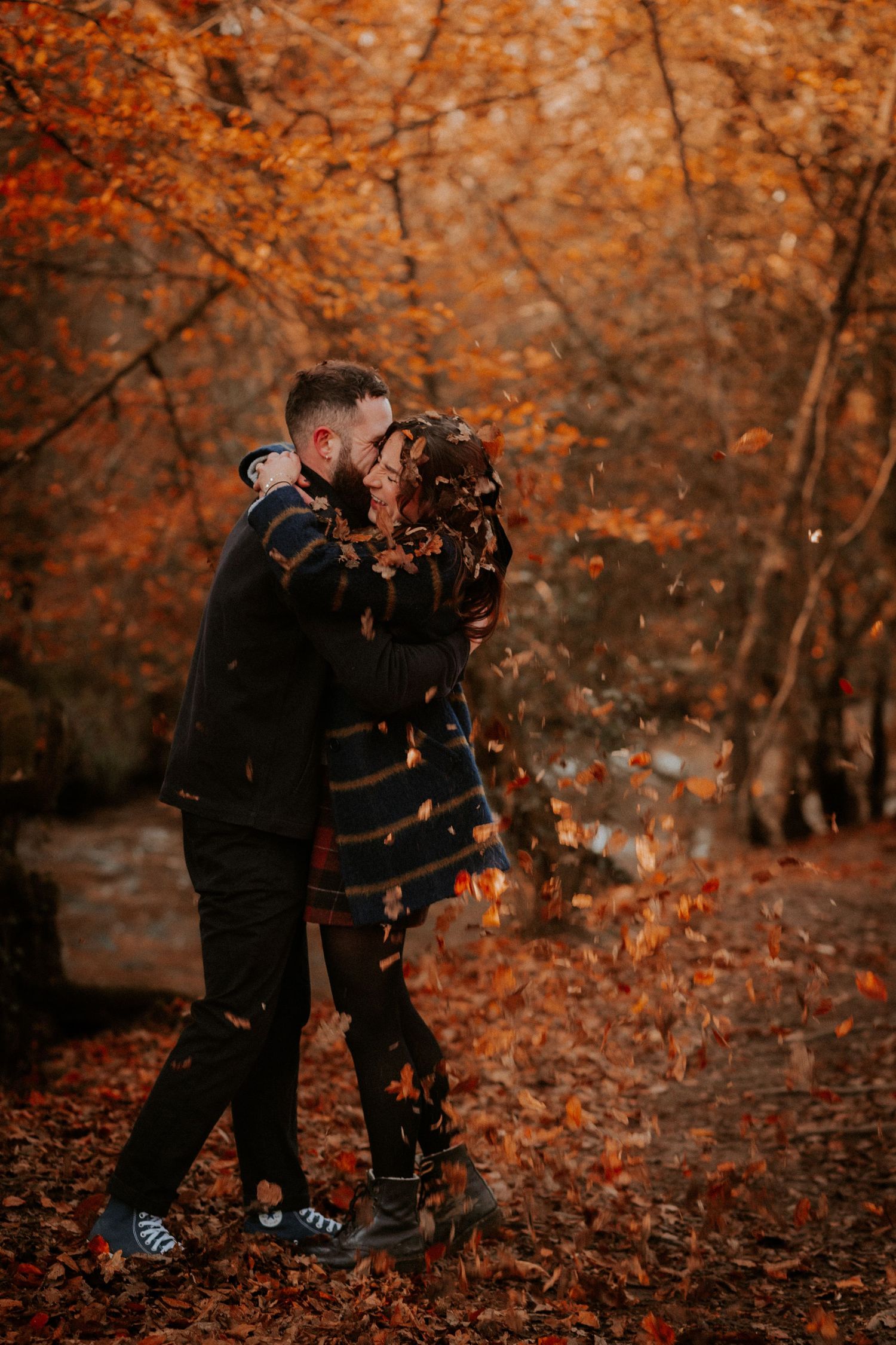 Couple embracing in autumn forest surrounded by vibrant orange foliage.