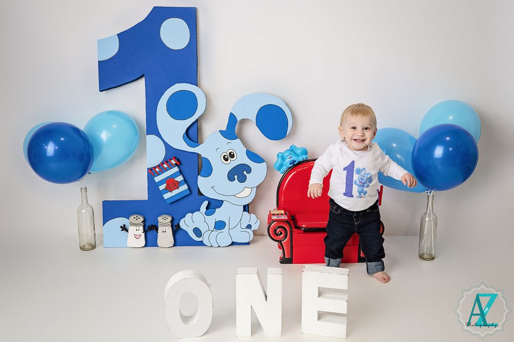 Child celebrating first birthday with Blues Clues themed decorations and blue balloons.