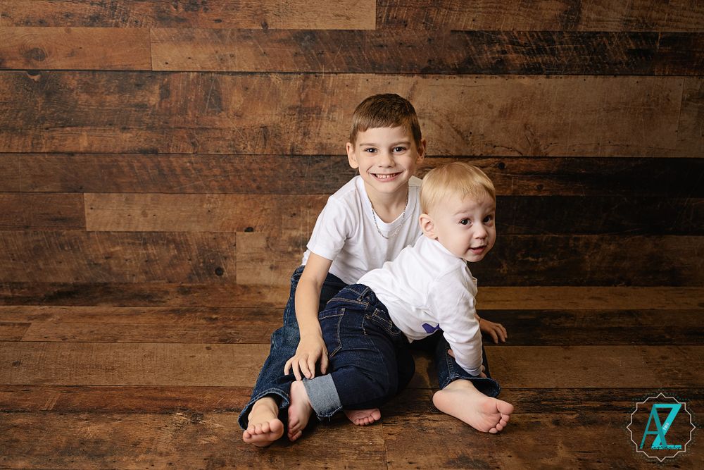Two children posed together against rustic wooden wall background in casual attire.