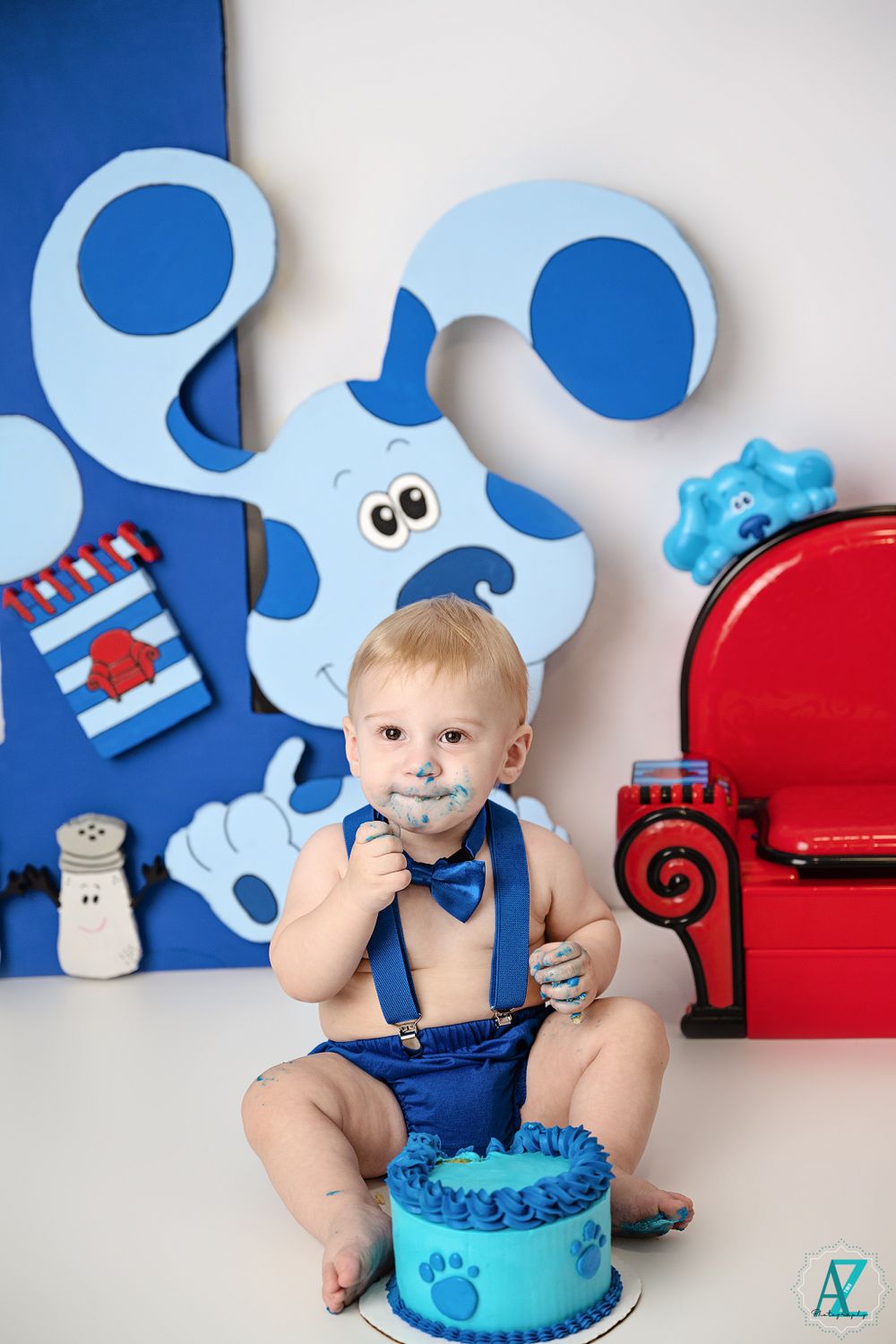 Blue and white first birthday party setup with a cake smash scene and decorative props against a light background.