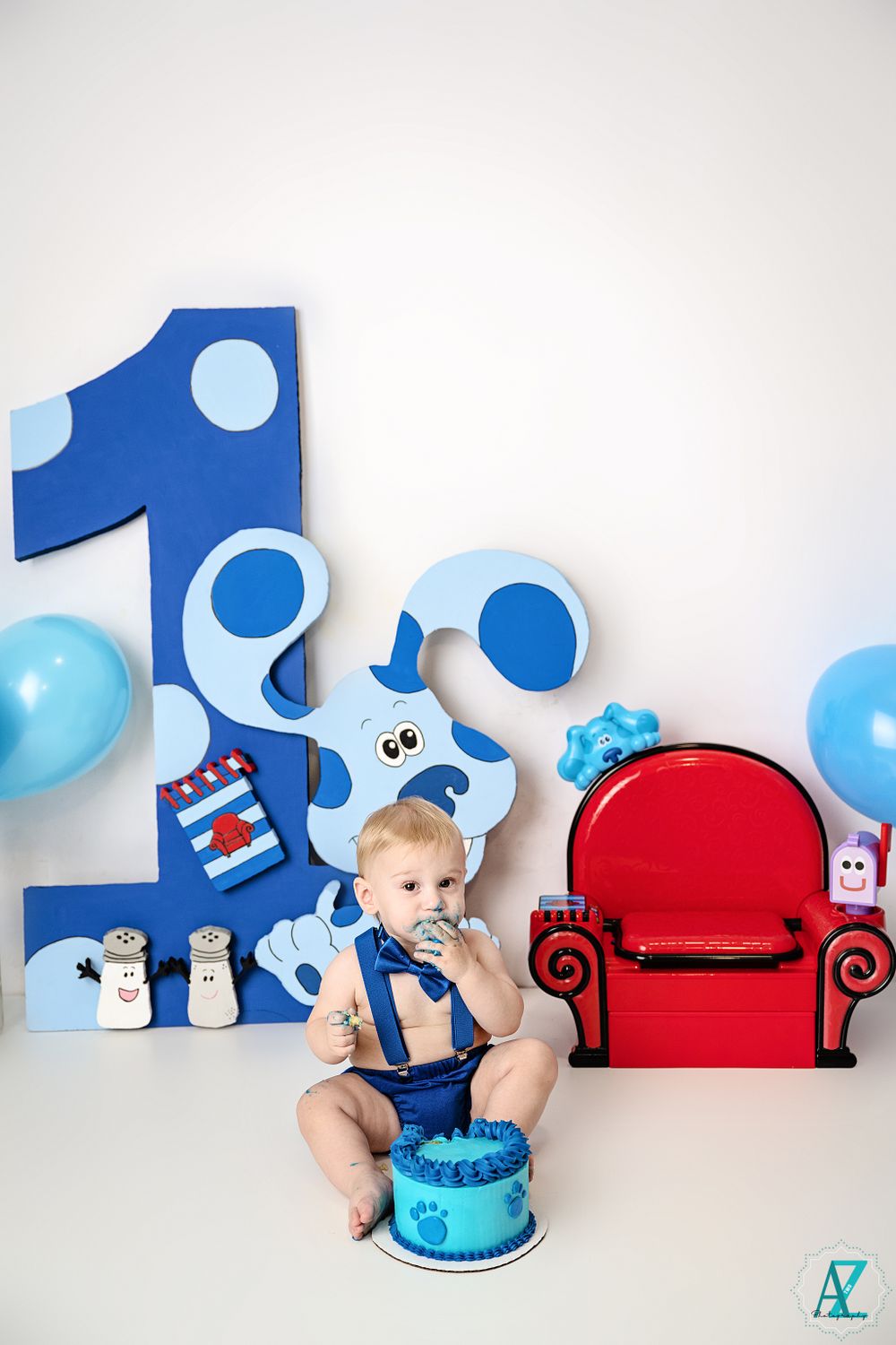 First birthday party scene with blue polka dot number one, red chair, and blue cake.