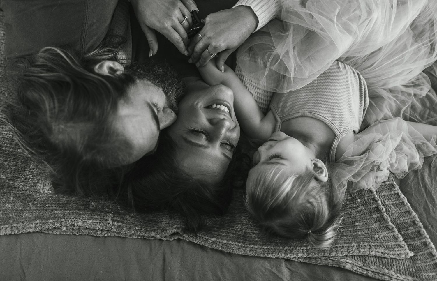 A black and white artistic portrait of three people lying together on a patterned carpet.