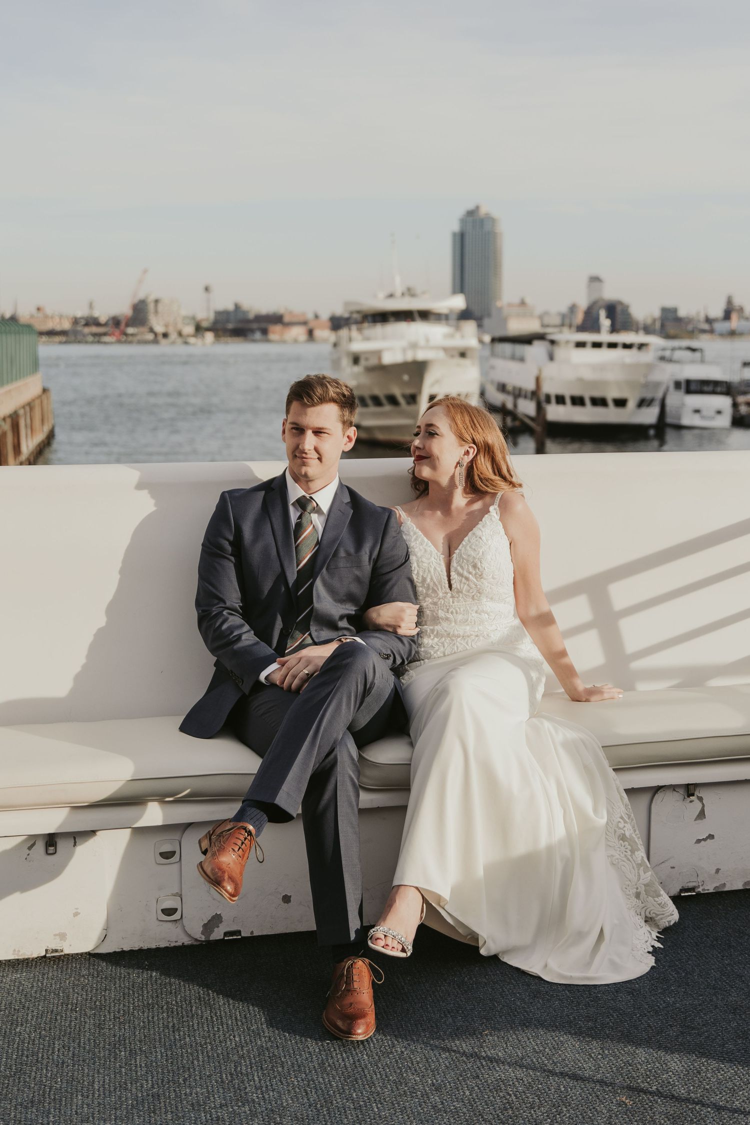 Newlyweds sitting together on boat deck overlooking city skyline.
