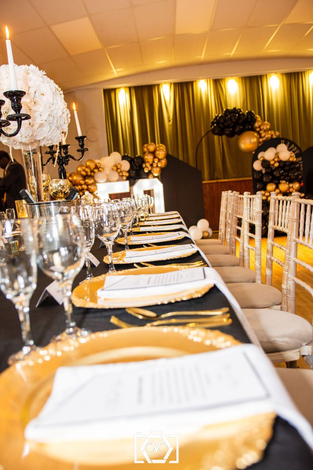 Elegant black and gold birthday dinner table setting with gold charger plates and floral centerpieces.