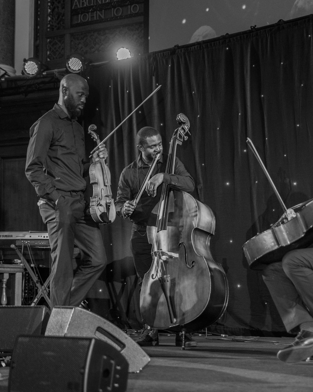 Black and white photo of jazz musicians playing double bass and violin on a church stage during a live concert.