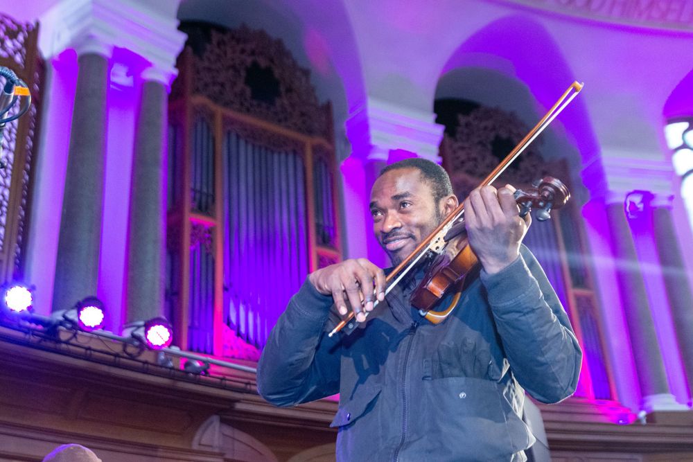 Smiling man playing violin in ornate church hall with purple lighting.