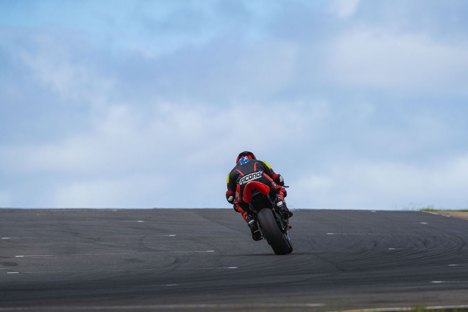 Motorcycle rider performs dramatic wheelie against cloudy sky on dark pavement.