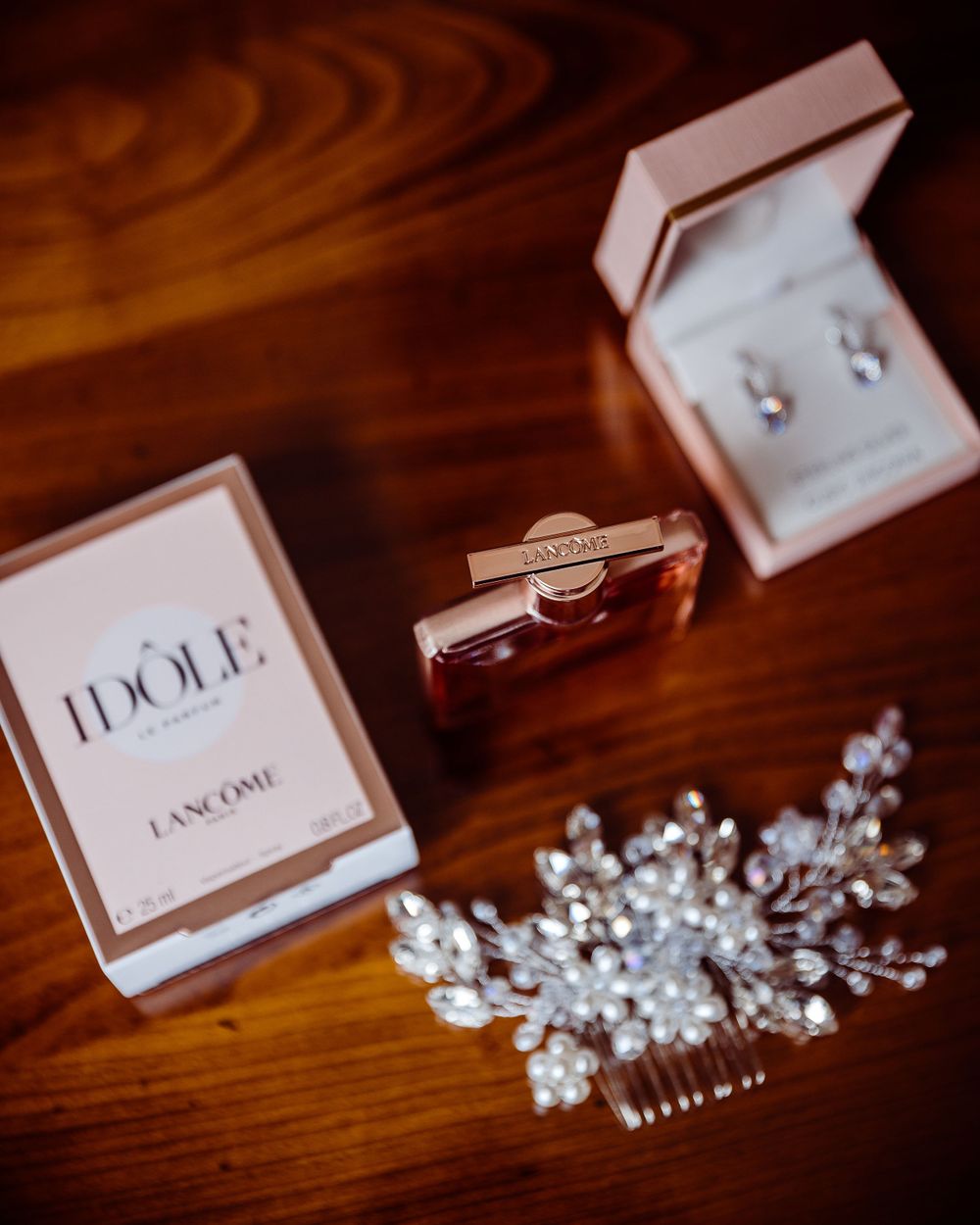 Wedding accessories including perfume, jewelry box and crystal hair piece on wooden surface.