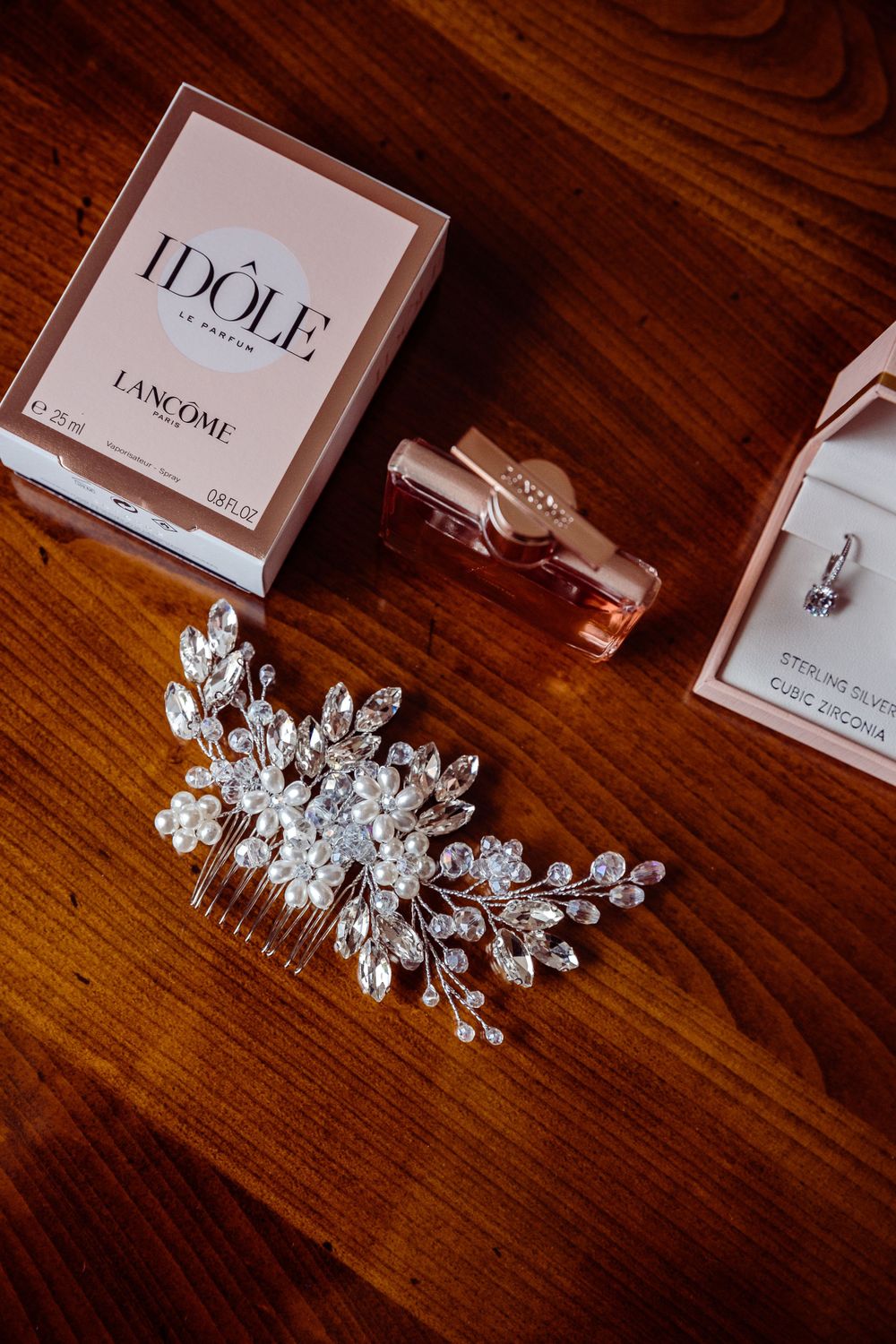 Wedding accessories including a Lancome Idole perfume bottle, jewelry hair comb, and accessories on wooden surface.