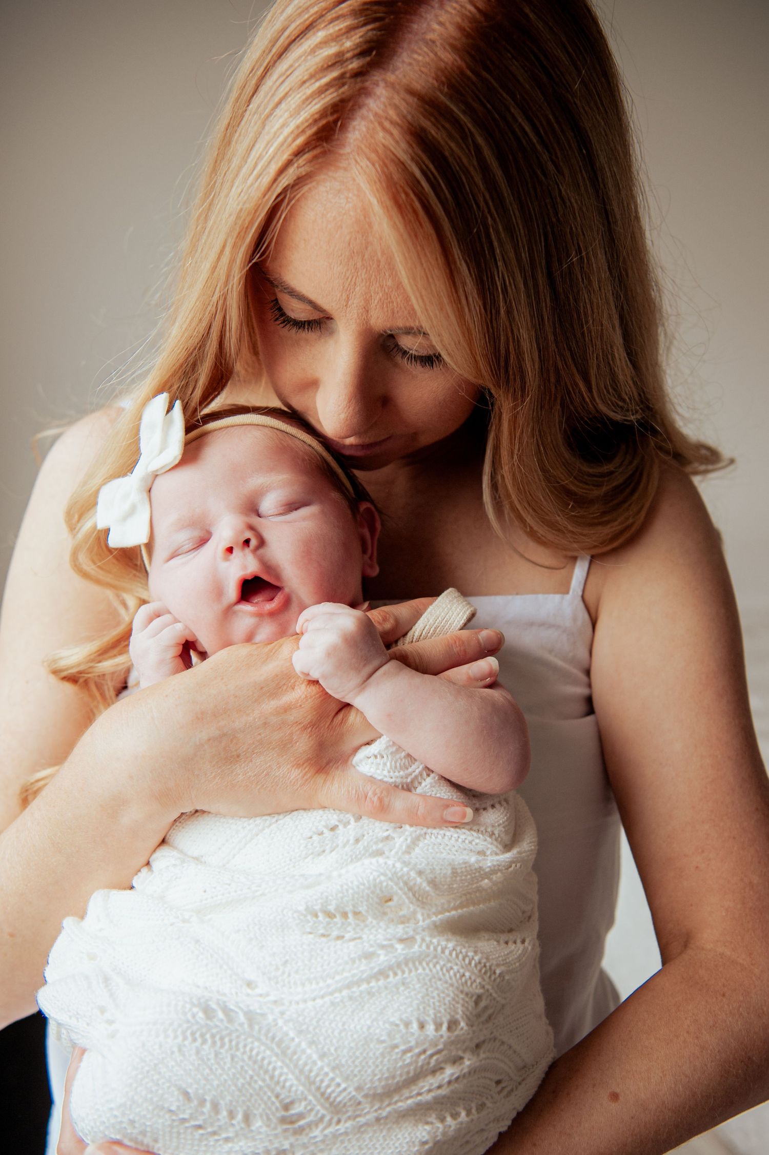 Sleeping newborn baby in white lace wrap with bow accessory being held by Mum.
Altona Family Photographer Melbourne