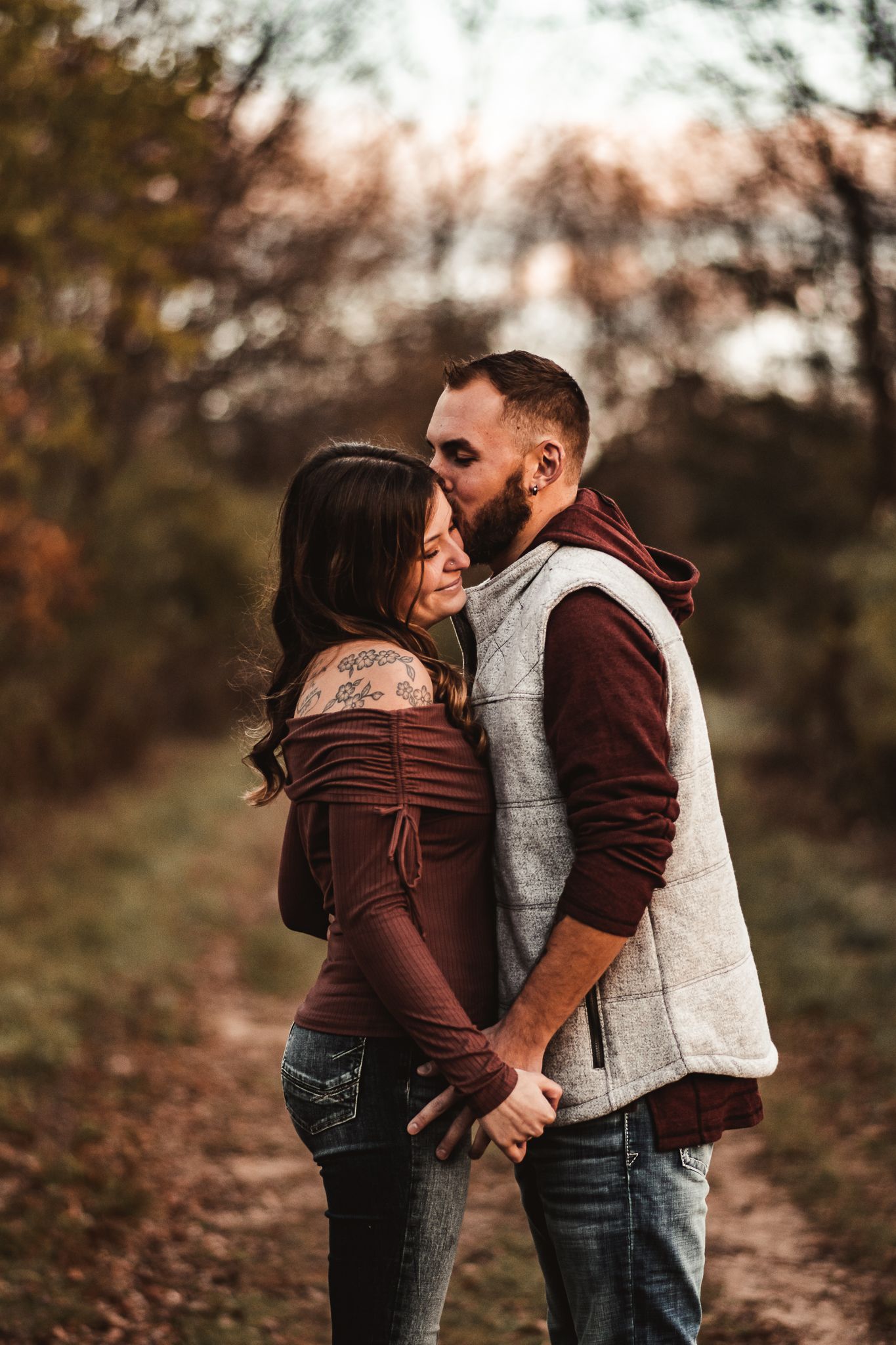 Intimate couple sharing tender moment on autumn forest path in coordinating burgundy and gray outfits.