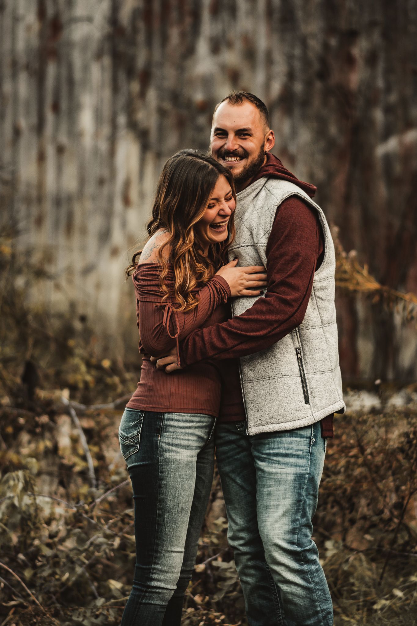 Happy couple sharing joyful embrace outdoors while wearing coordinated burgundy and gray clothing.