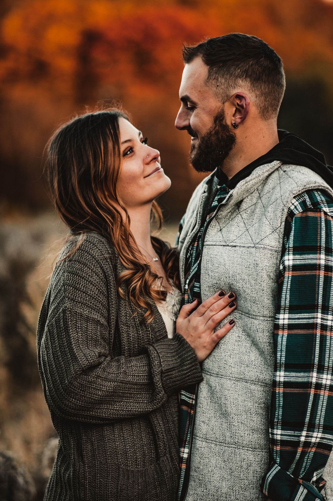 A loving couple in casual winter attire gazing at each other against an autumn backdrop.