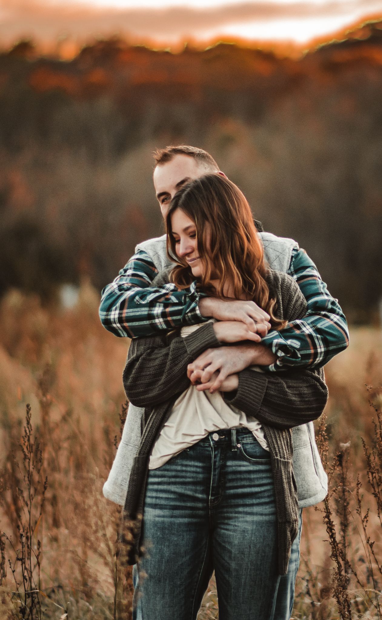 A romantic embrace in autumn field during golden hour with warm sunset lighting.