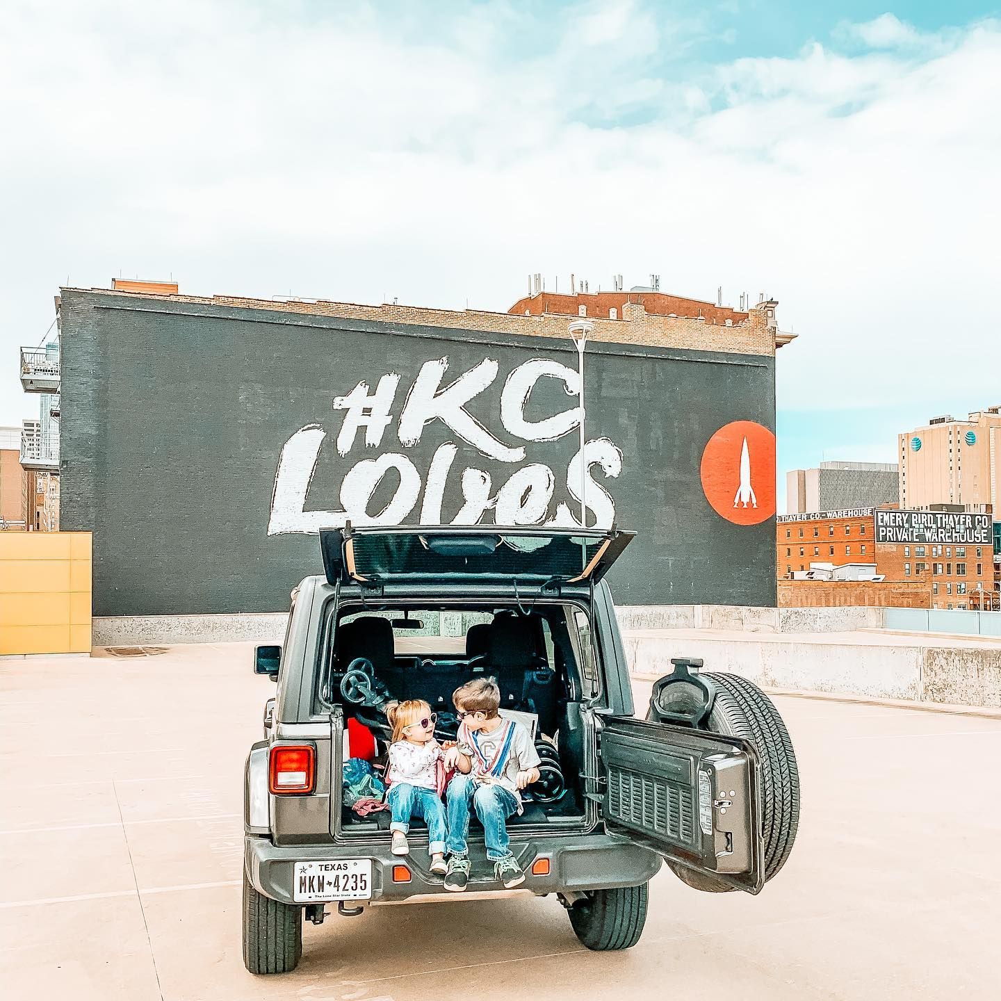 Black pickup truck parked in urban setting with graffiti wall and city buildings in background.