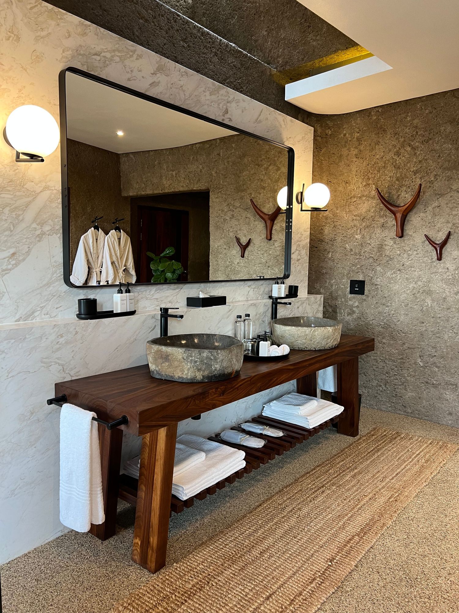 Rustic modern bathroom vanity with stone vessel sinks, wooden console and large framed mirror.