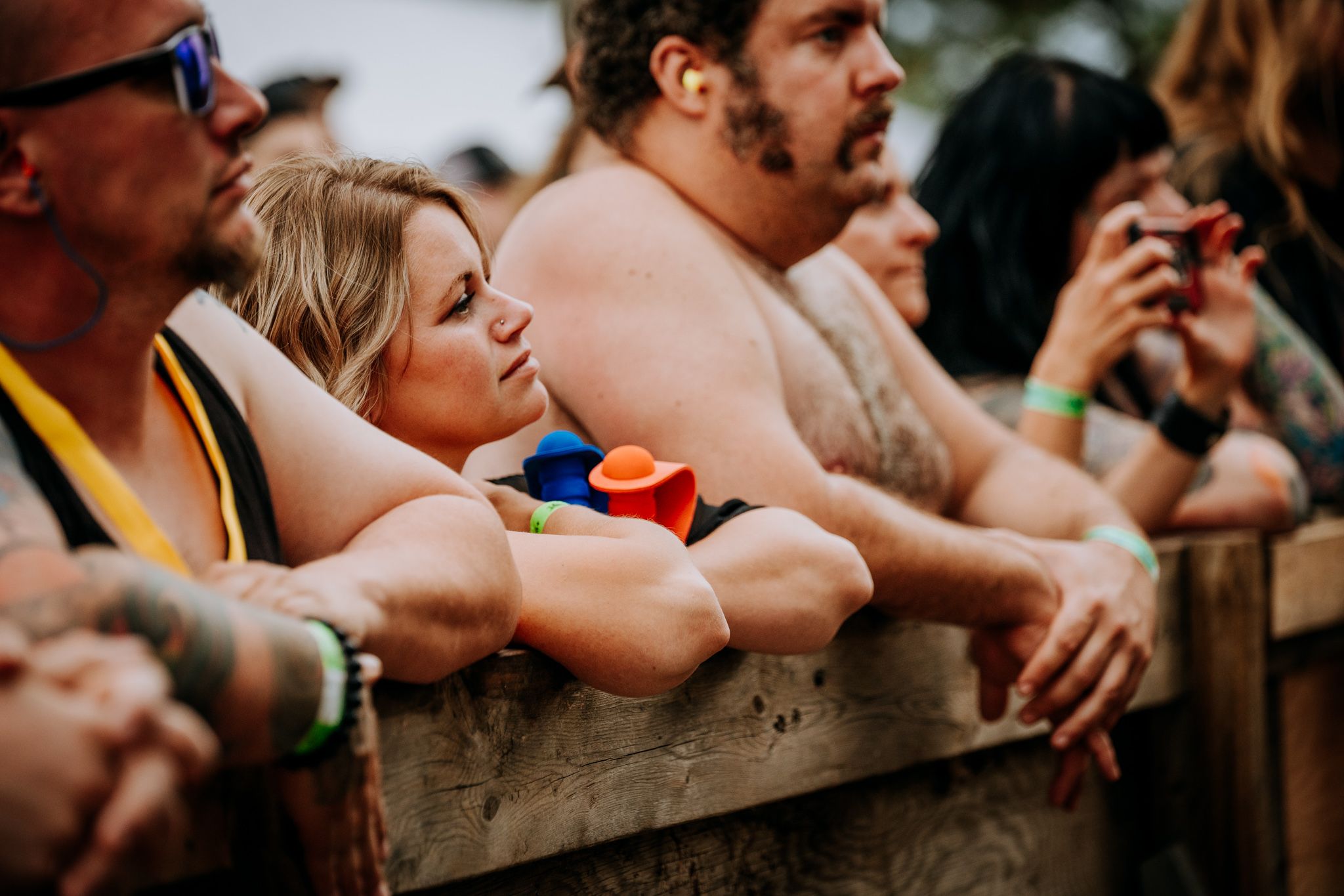 Festival attendees relaxing against wooden barrier during outdoor concert event.