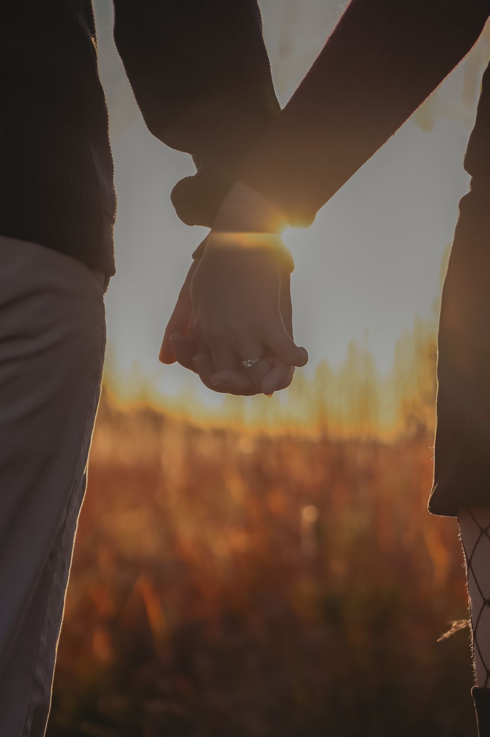 Silhouette of clasped hands against golden sunset background.