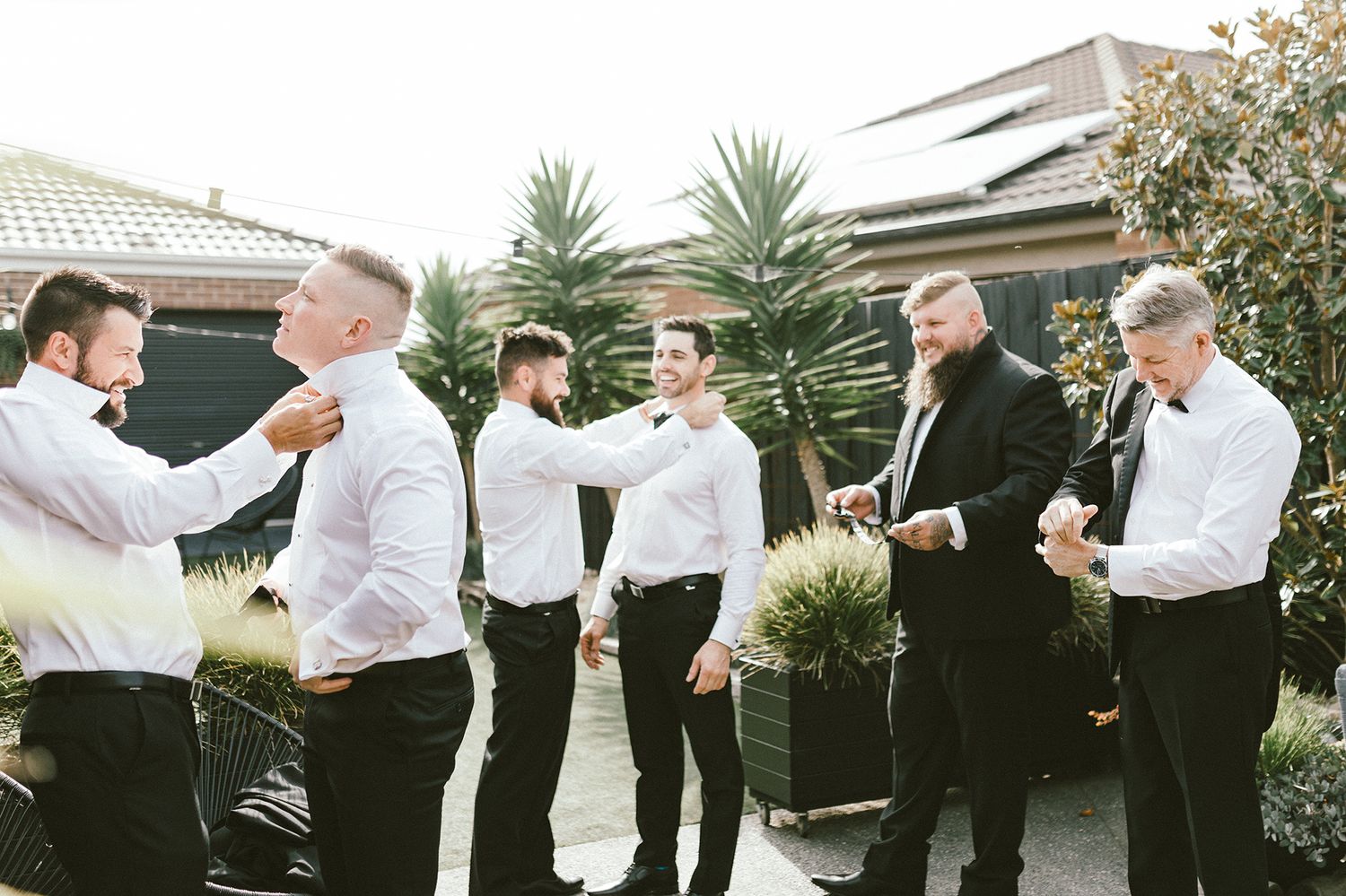 A group in formal white shirts and black pants gathered outside near palm trees.
