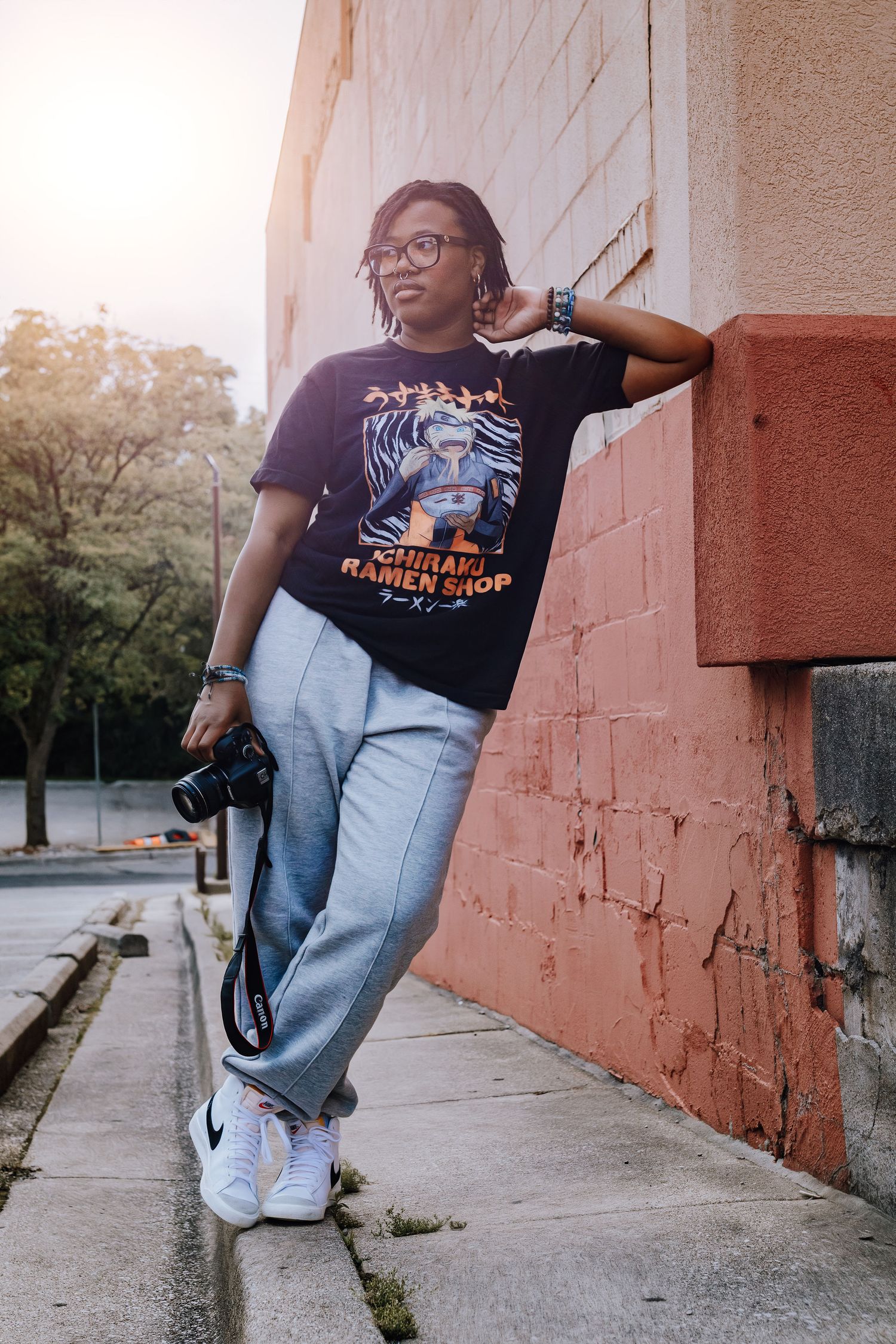 Urban photographer in casual streetwear poses against pink wall with camera.