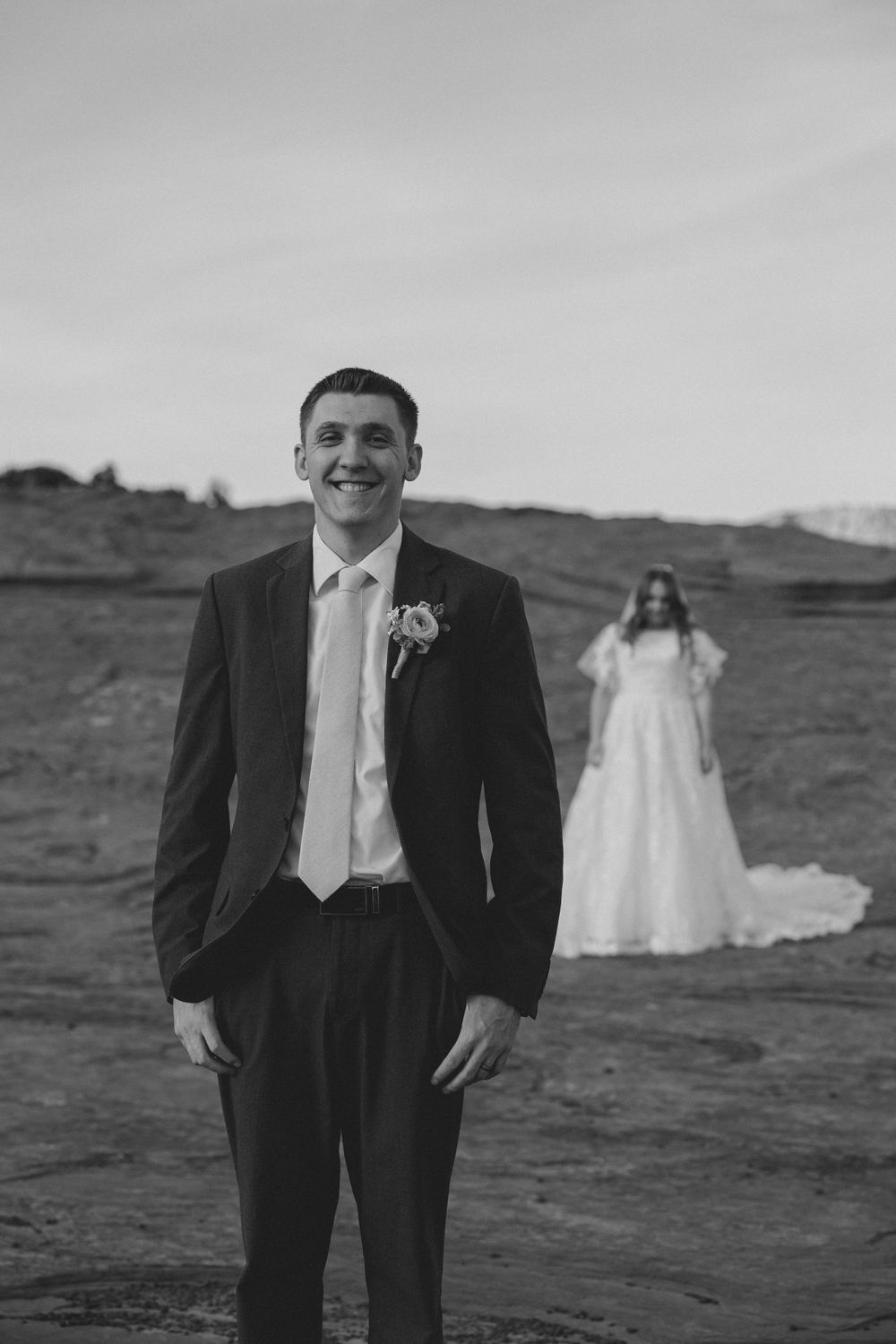 A black and white wedding photo with desert landscape in background.