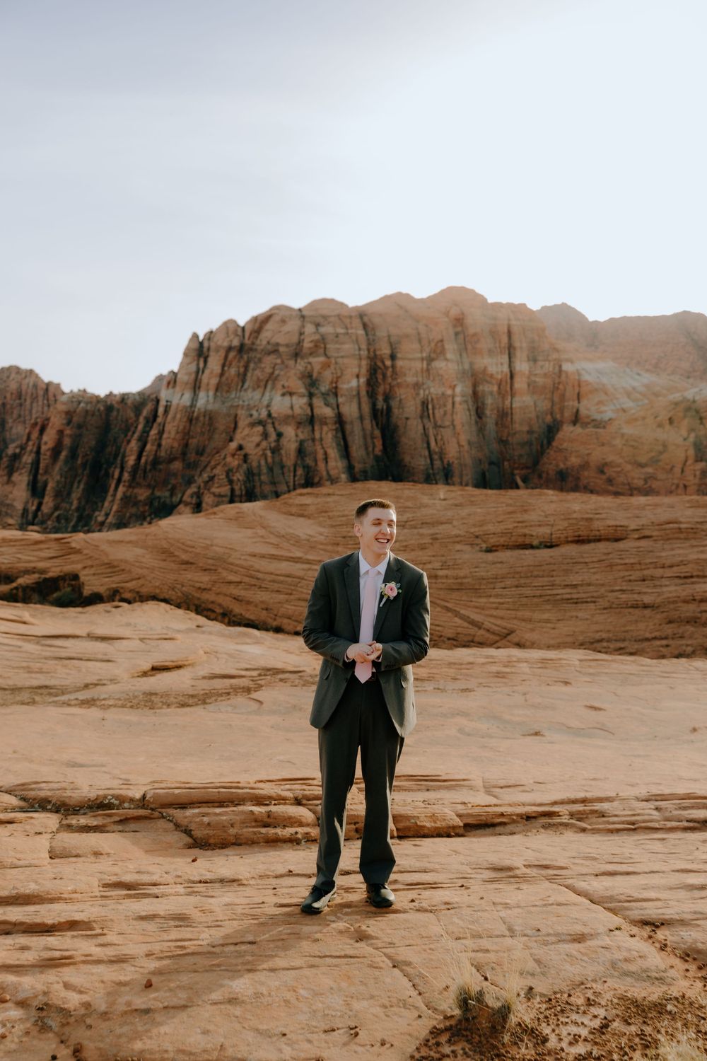 Wedding portrait of a groom standing on red rock terrain with canyon walls behind.